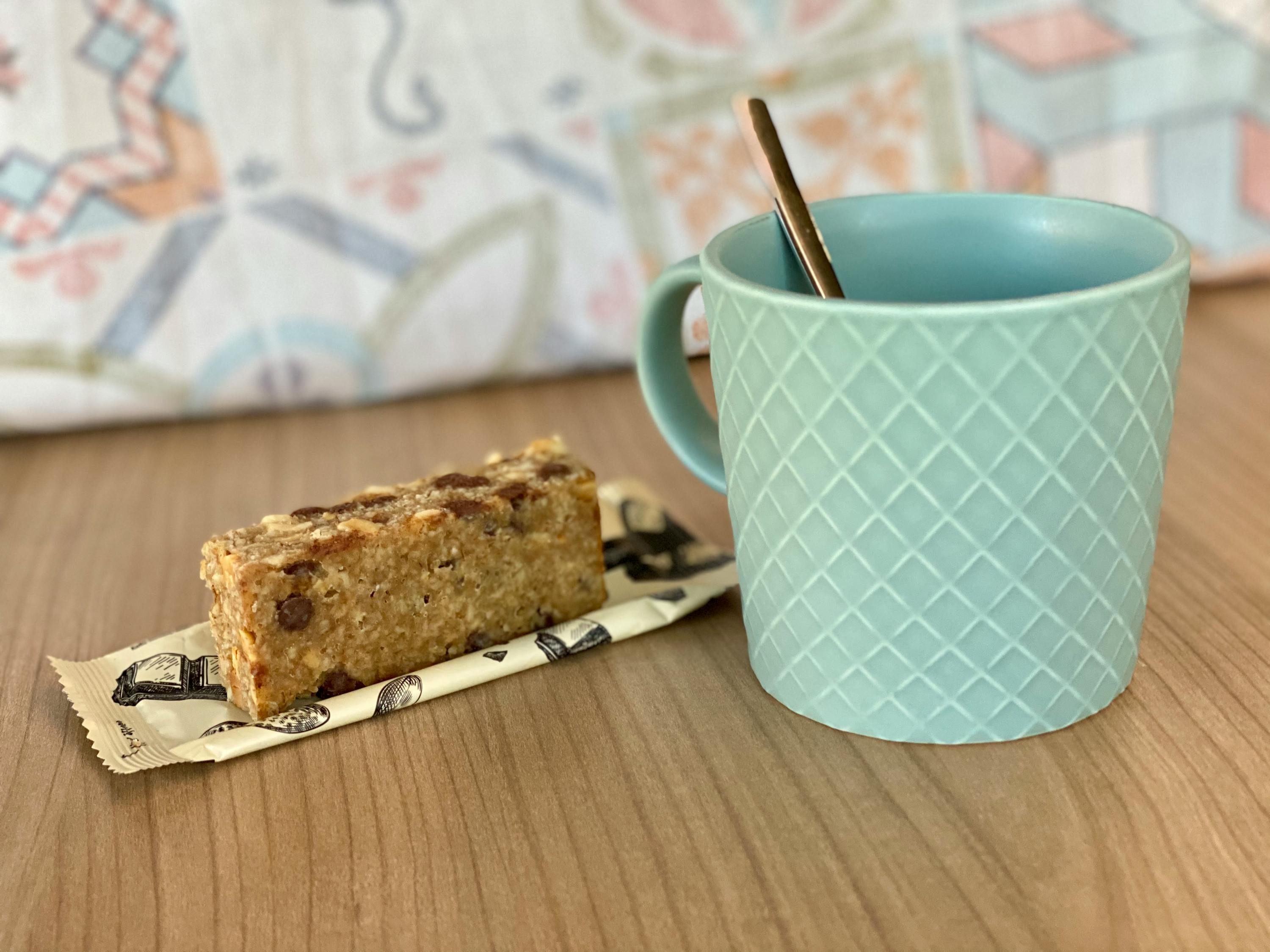 una barretta di granola con gocce di cioccolato accanto a una tazza di caffè