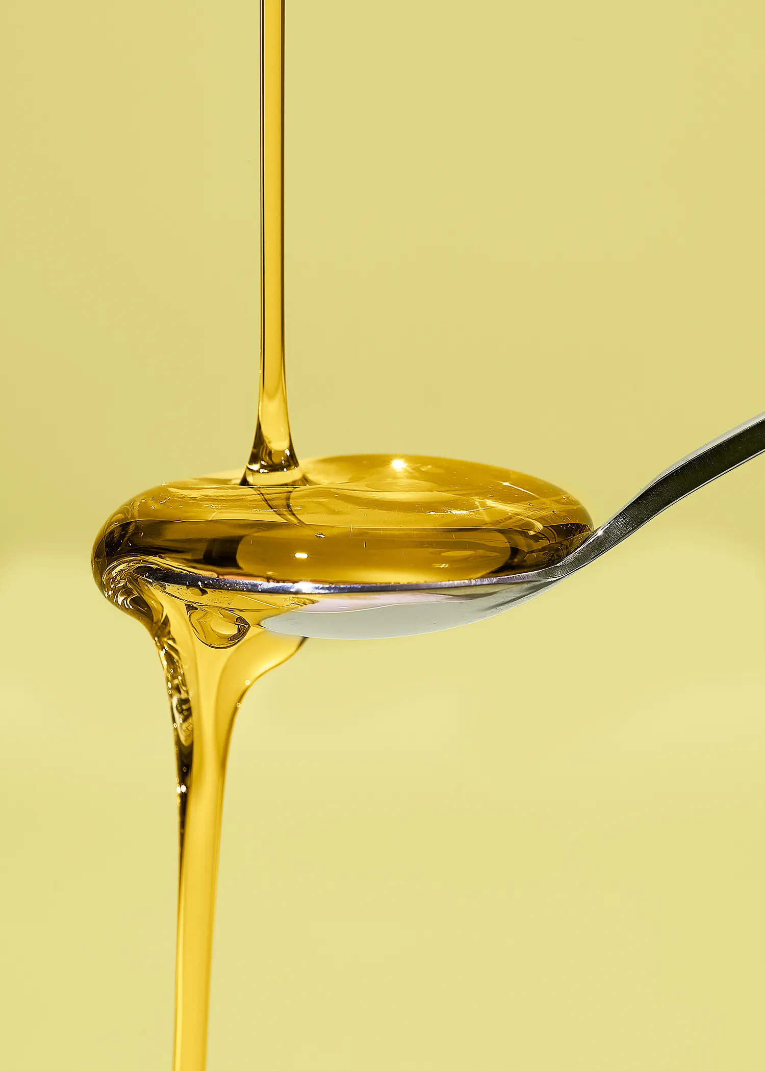 du miel doré coule en un filet continu sur une cuillère en métal sur un fond jaune.
