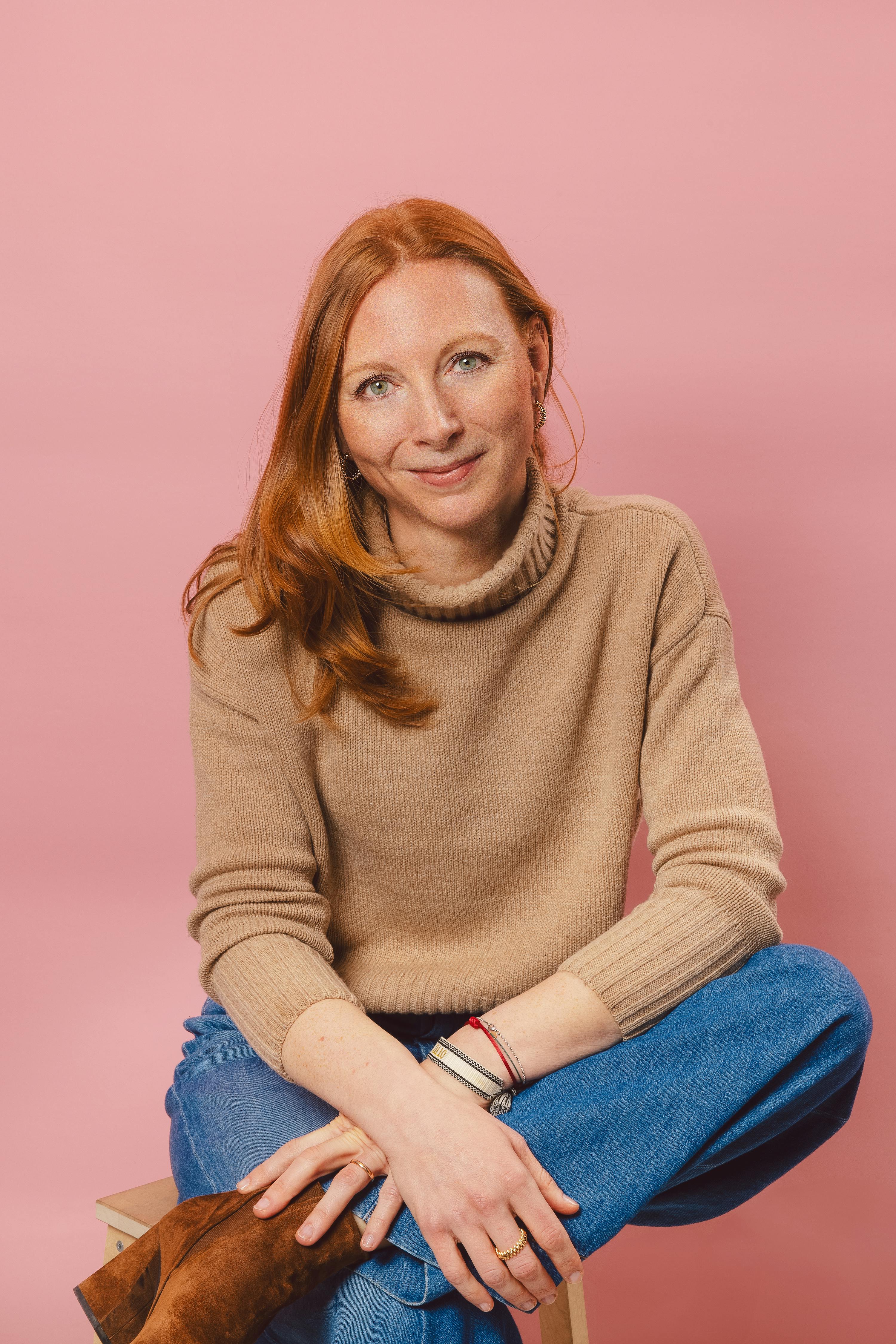 Eine Frau sitzt mit ihren Beinen auf einem Stuhl und trägt einen Pullover und Jeans