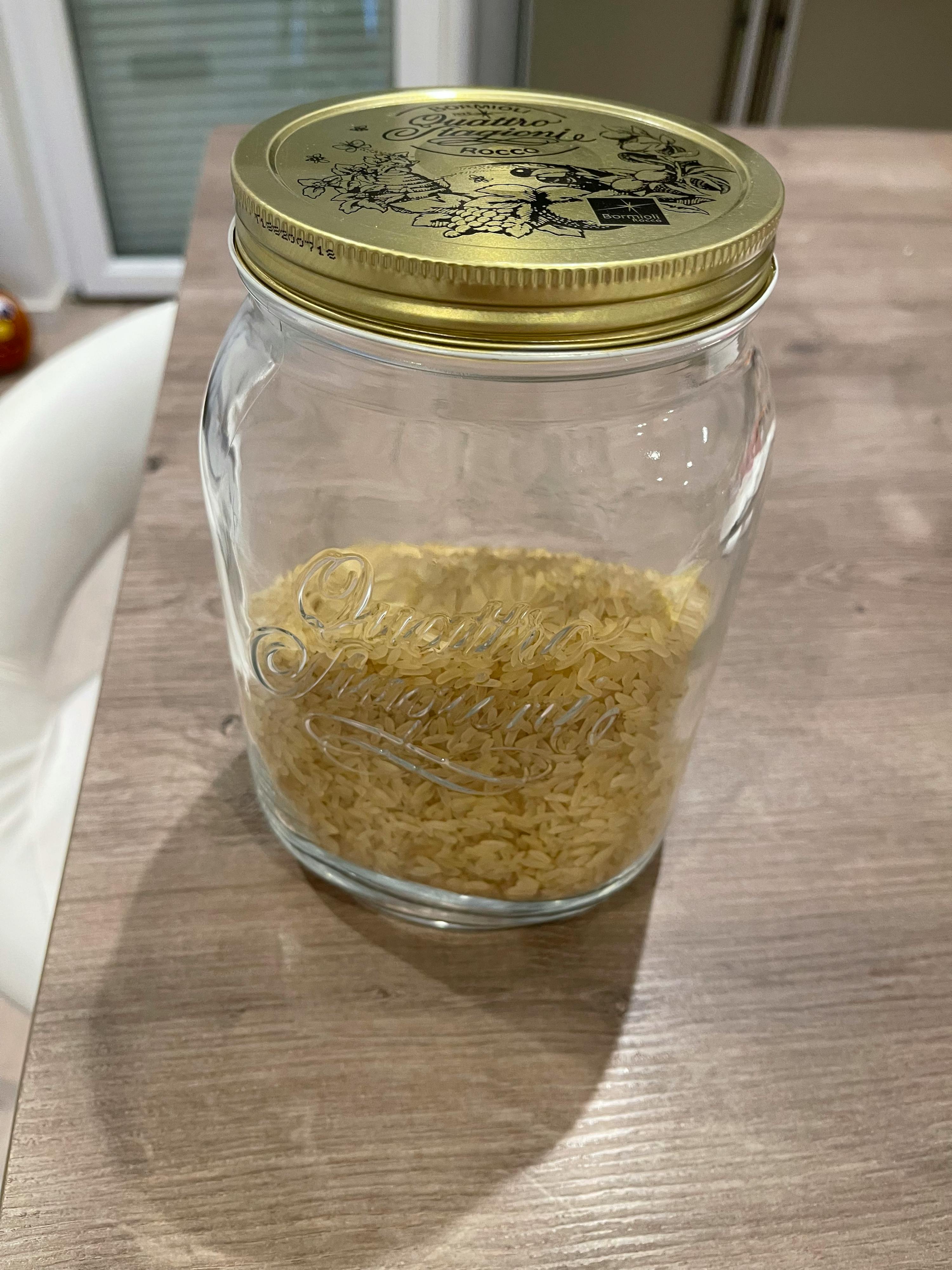 un bocal en verre rempli de riz est posé sur une table en bois