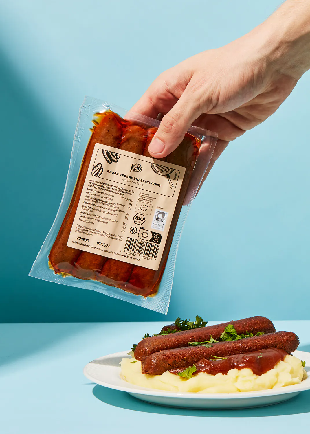 une personne tient un sac de saucisses végétales sur une assiette de purée de pommes de terre