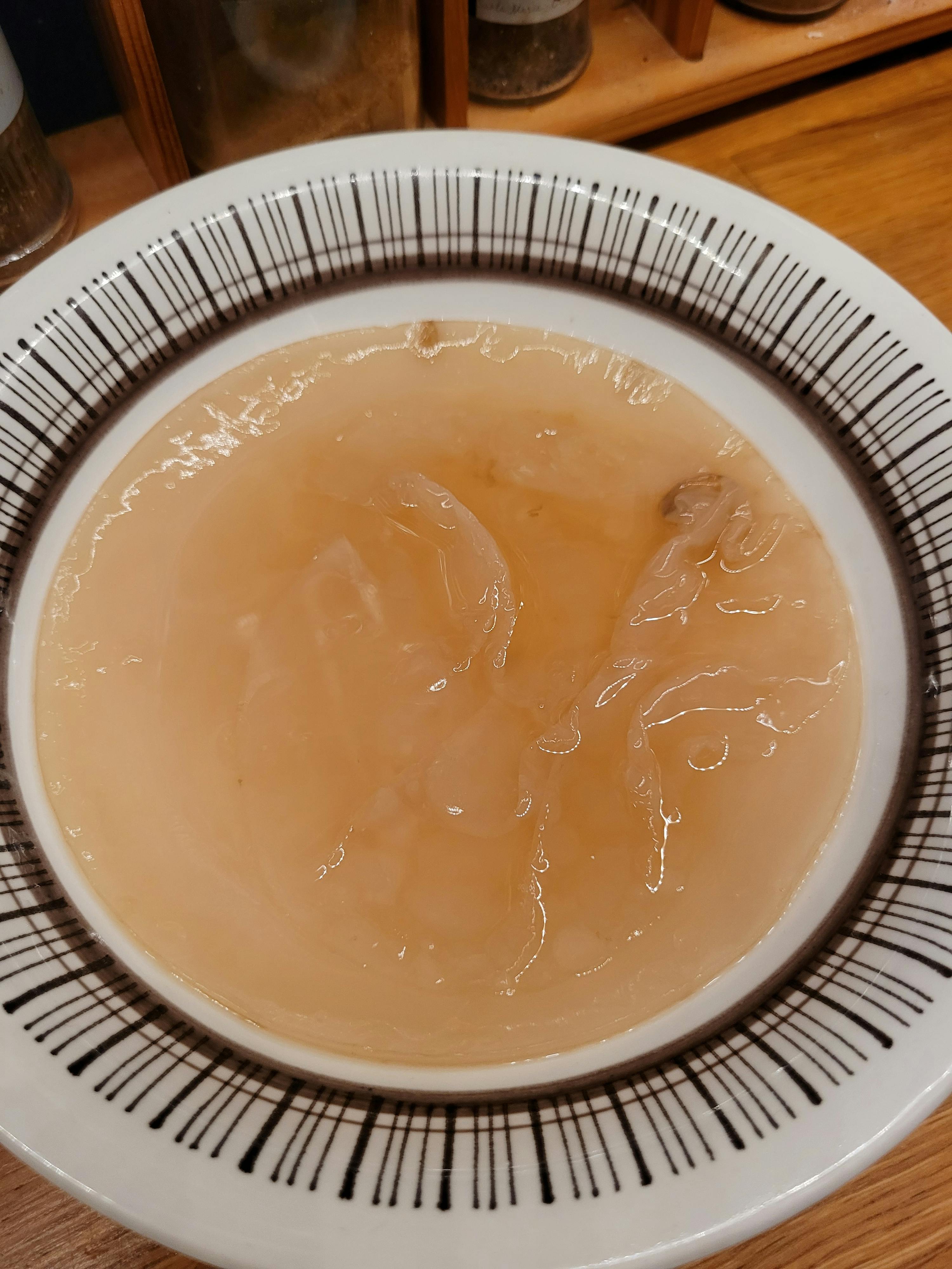 a close-up of a thick, translucent, peach-colored scoby floating in a white bowl with black stripes.