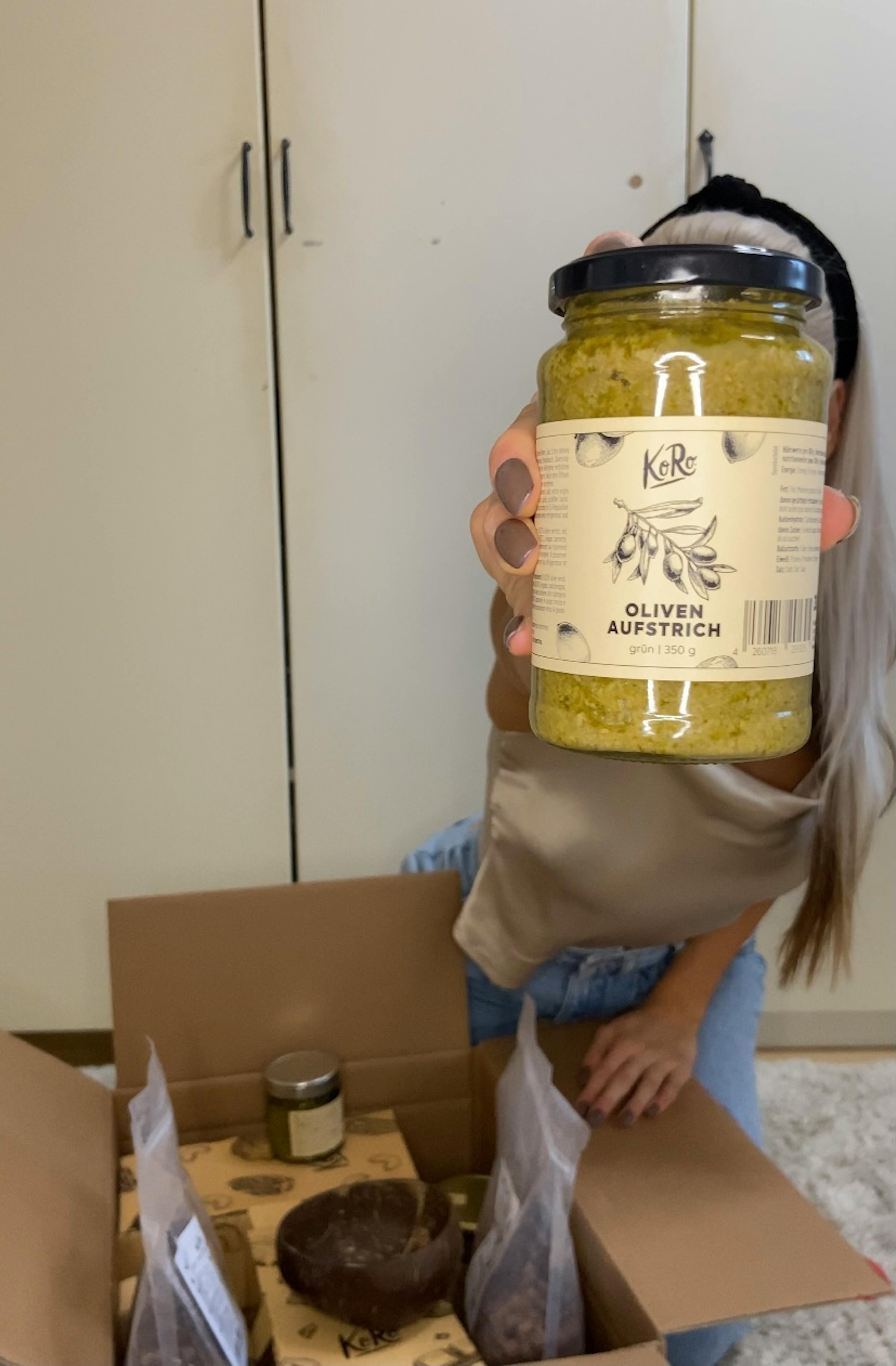 eine Frau hält ein Glas oliven aufstrich in ihren Händen