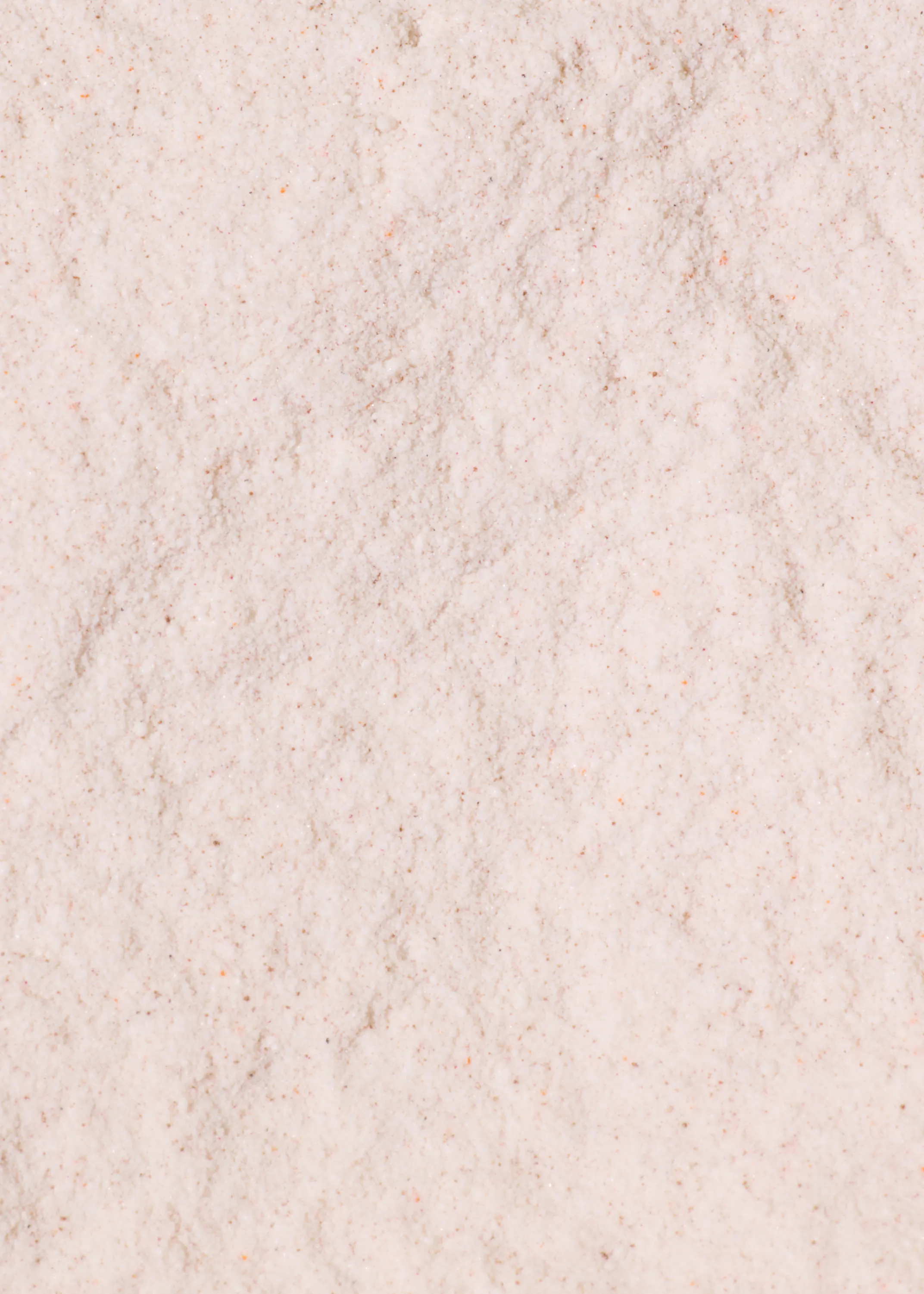a full frame close-up of light pinkish-beige granular powder with tiny reddish-brown specks.