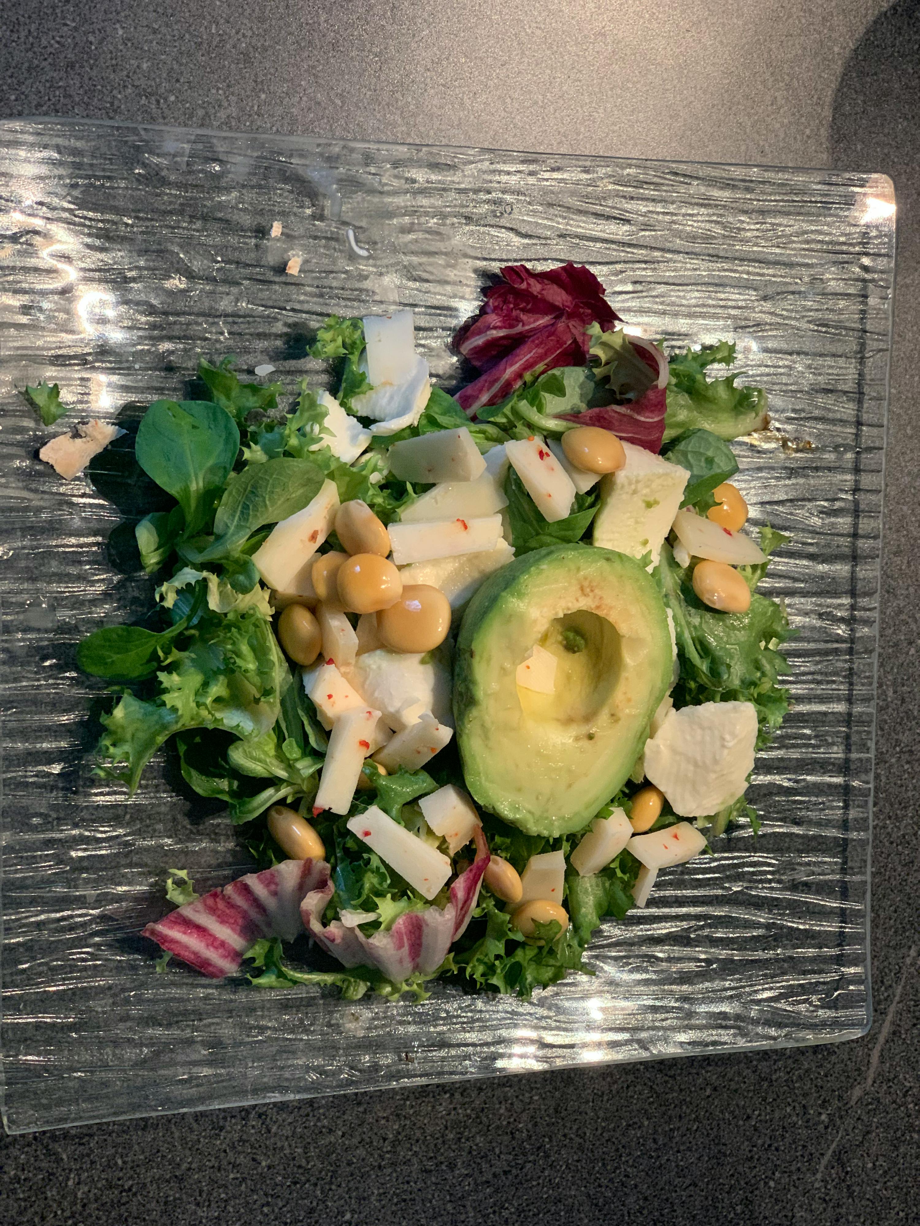une assiette en verre remplie d' une salade avec un avocat au milieu
