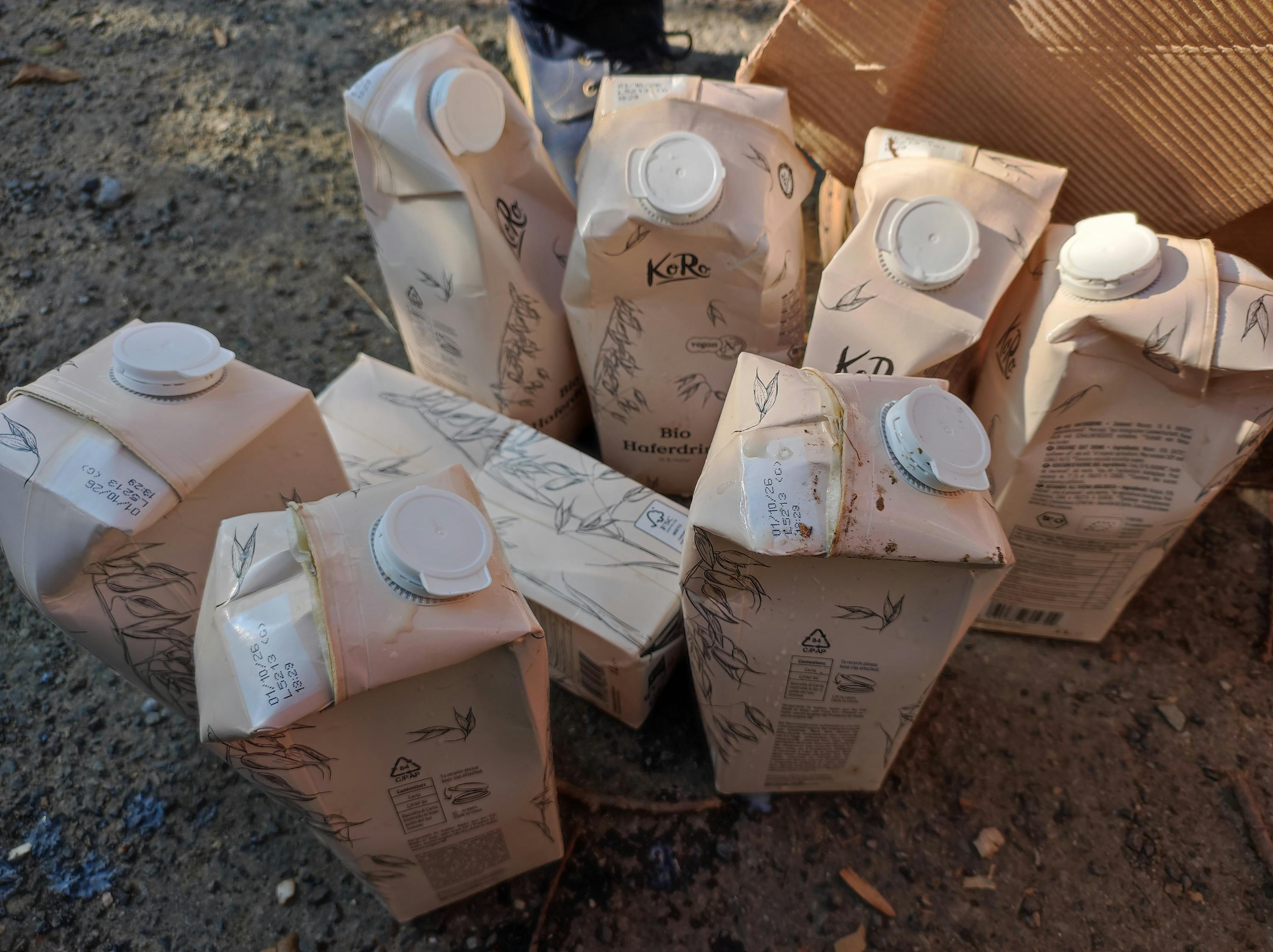 plusieurs cartons de boisson à l'avoine koro bio haferdrink, certains légèrement endommagés, sont visibles sur le sol et dans un sac en papier.