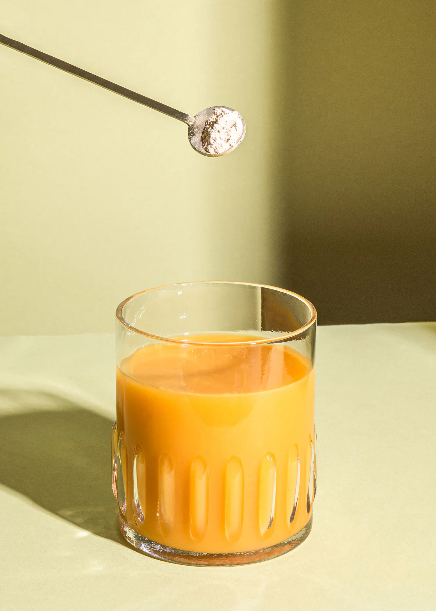 a spoonful of powder is being poured into a glass of orange liquid