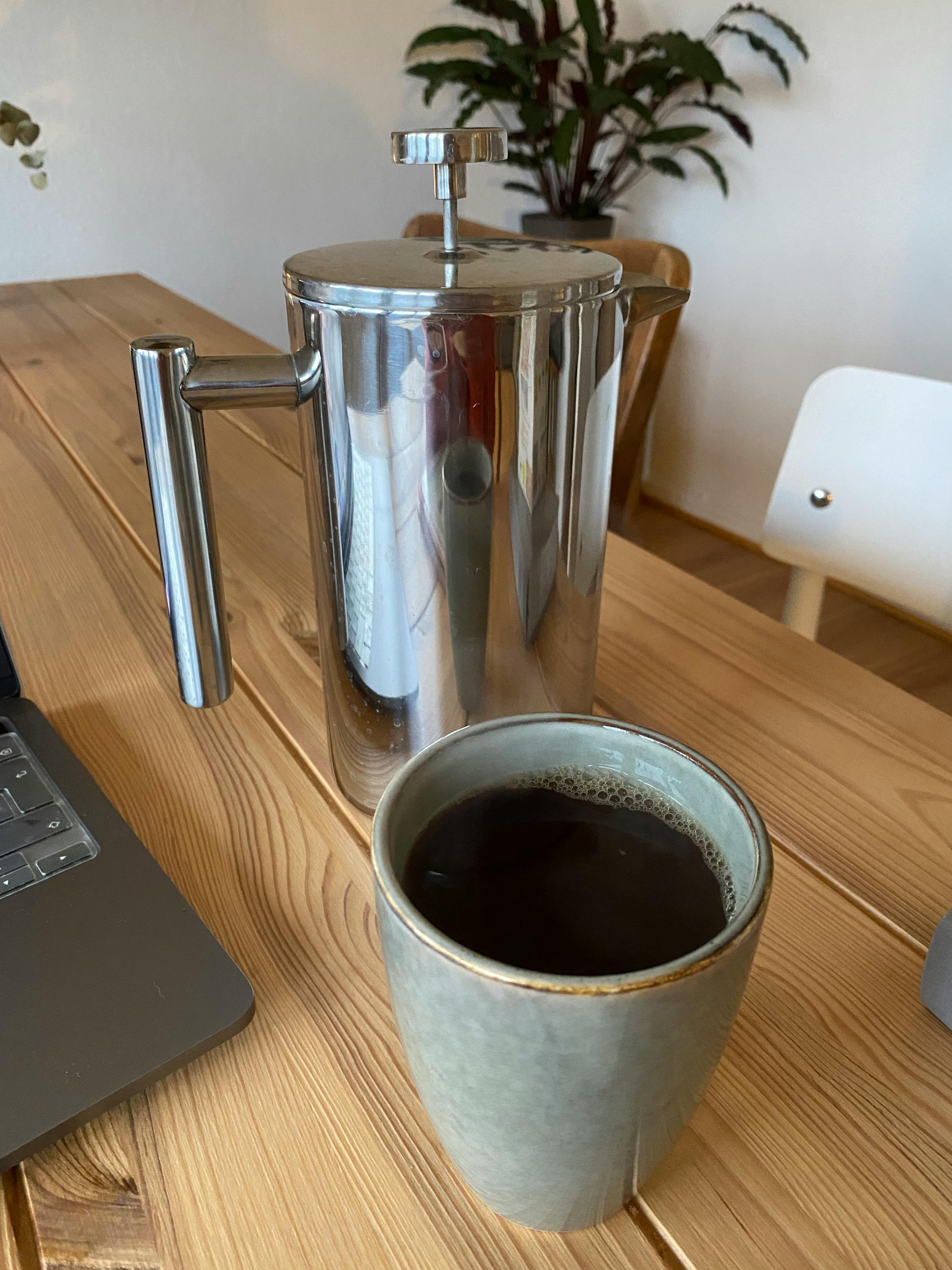 a french press sits next to a cup of coffee on a wooden table