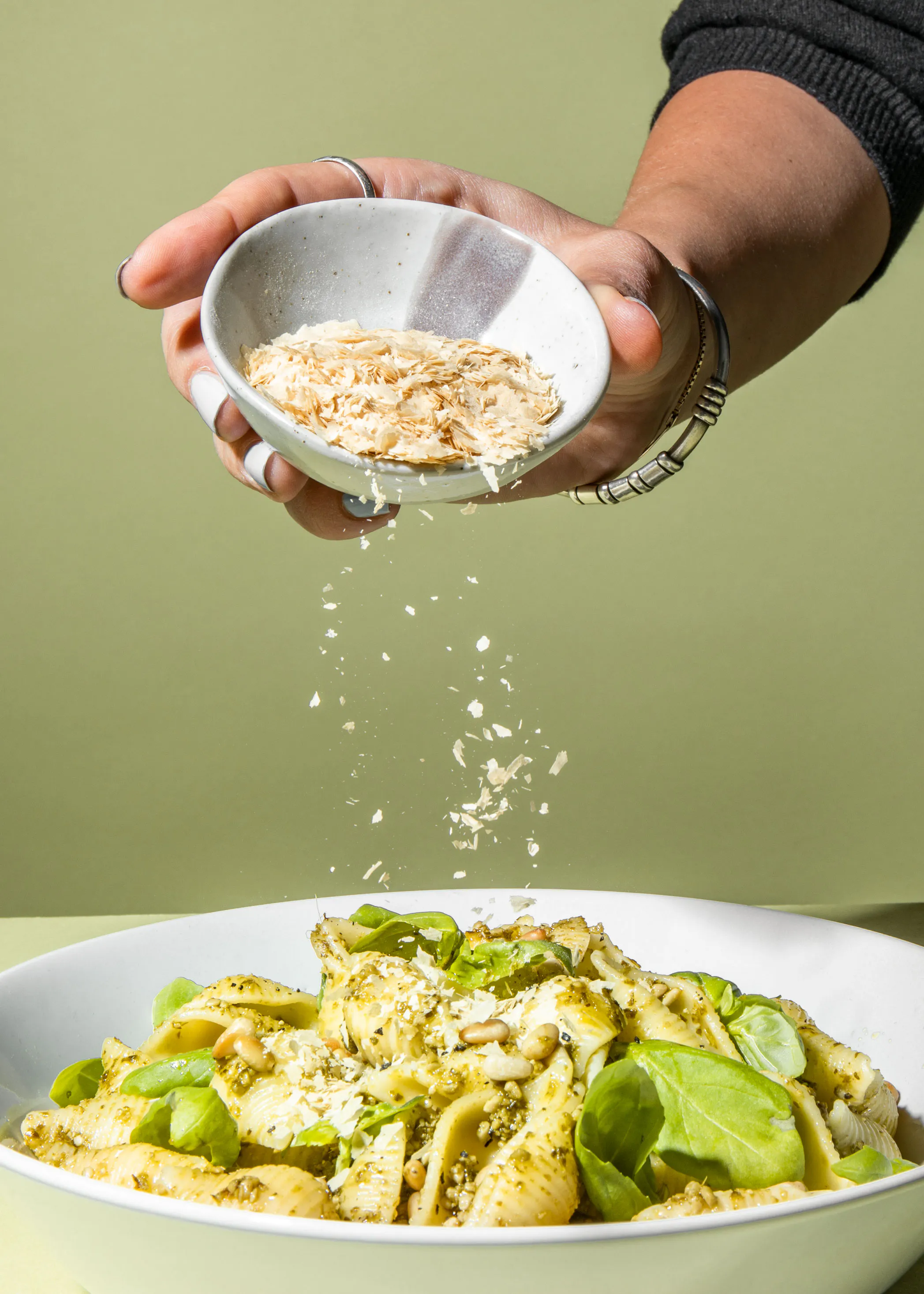 une personne verse du parmesan sur une assiette de pâtes