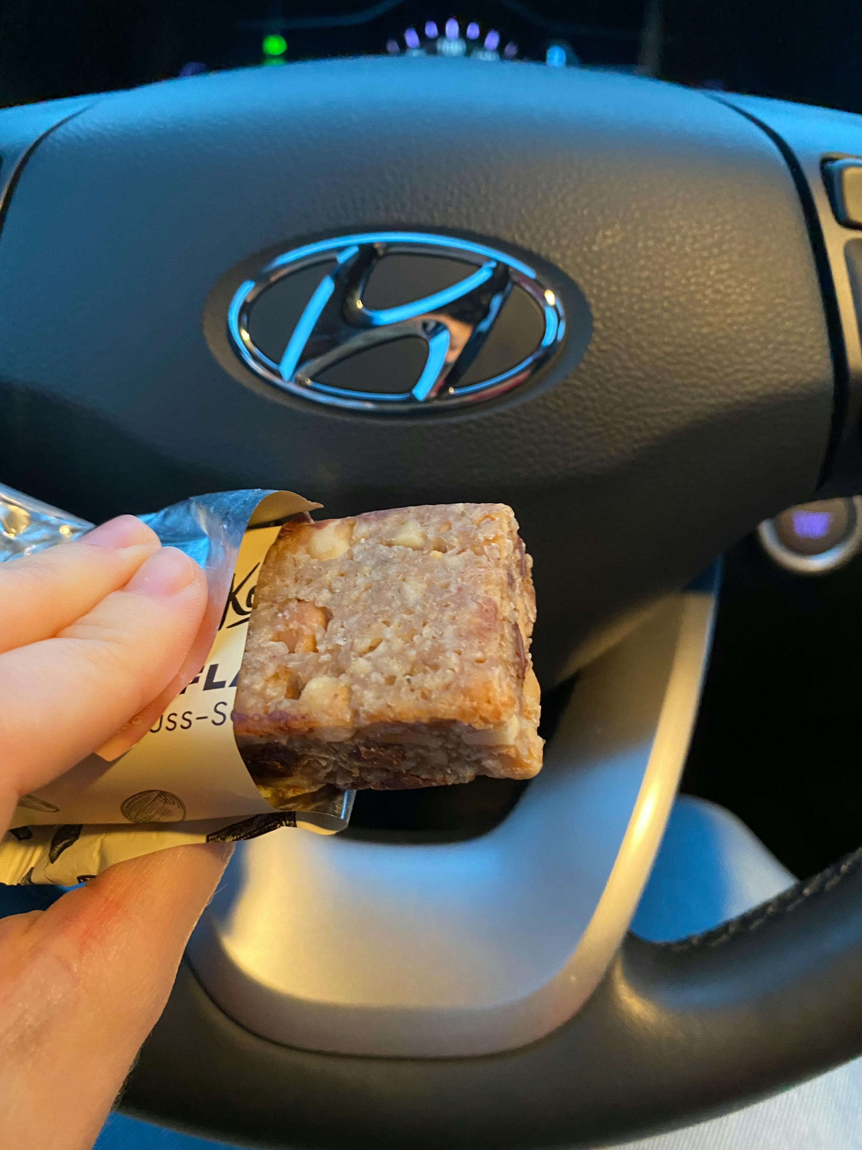 una persona tiene in mano una barretta di cioccolato con il logo di una hyundai sullo sfondo