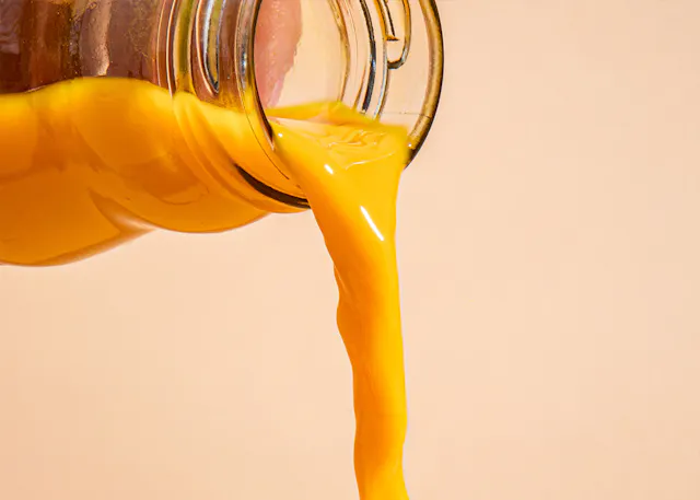 gelber Saft wird aus einem Glasbehälter gegossen