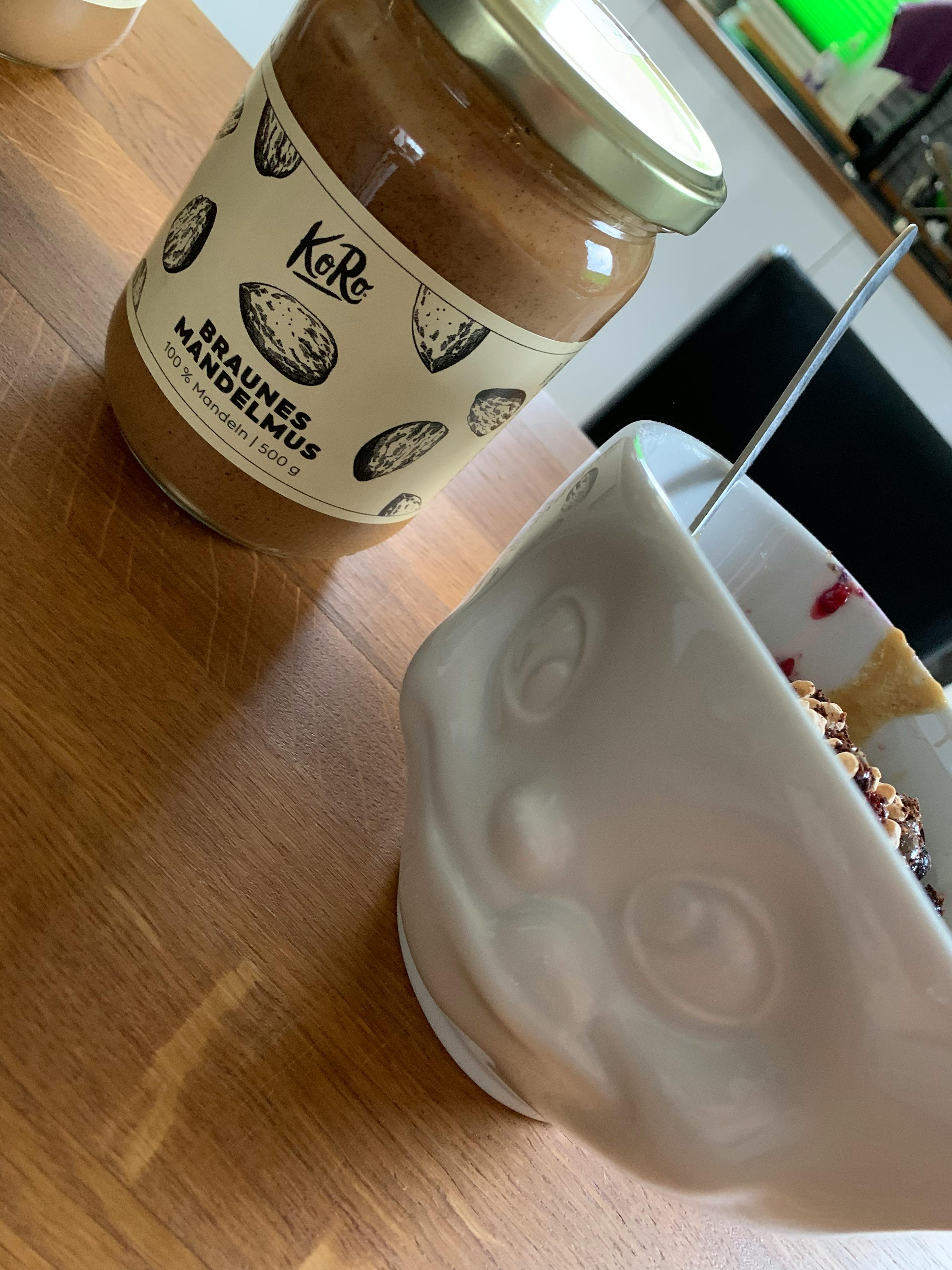 ein Glas braunes Mandelmus steht neben einer Schüssel mit Müsli