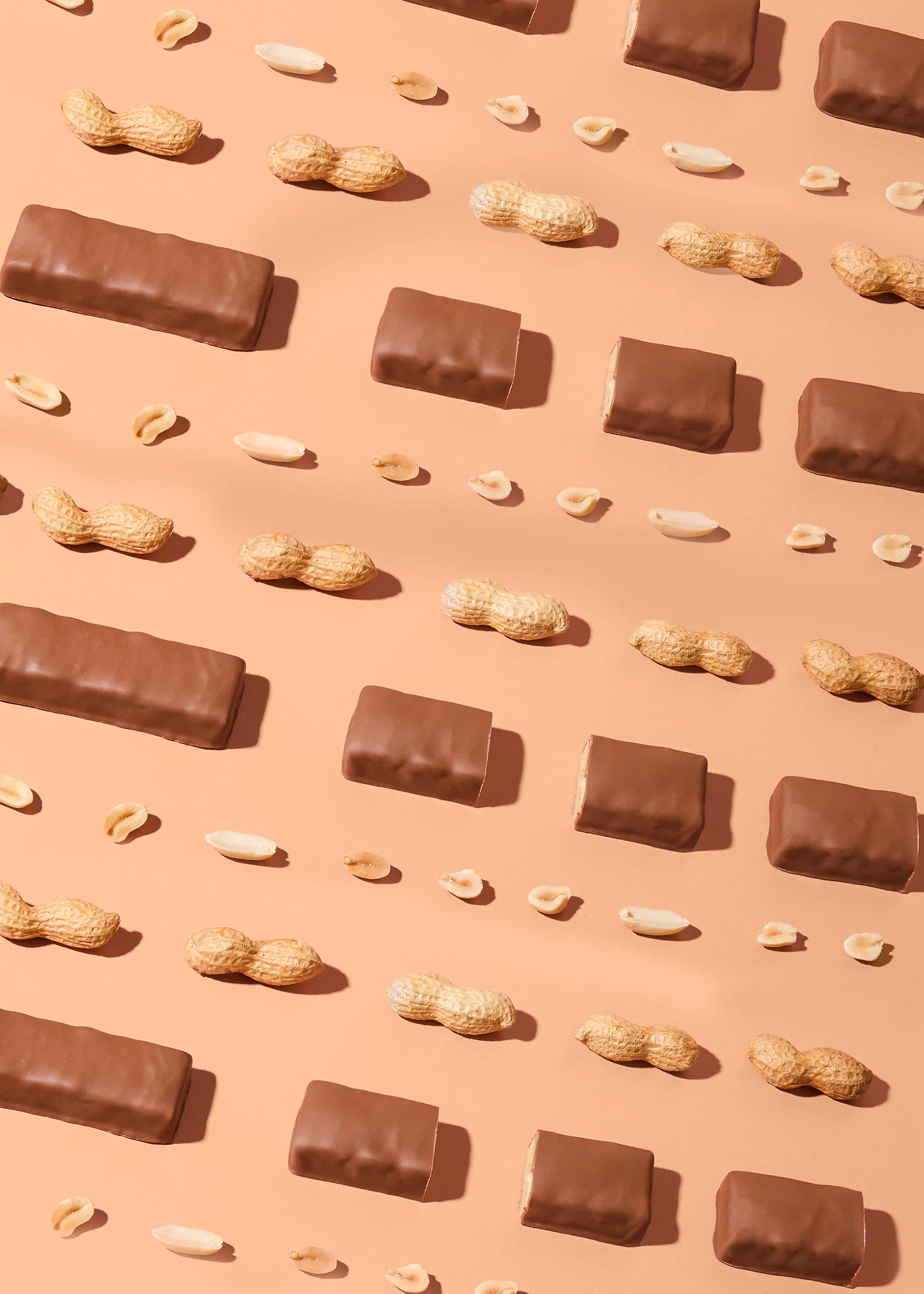 motif répétitif de barres chocolatées et de cacahuètes (avec et sans coque) sur un fond beige.