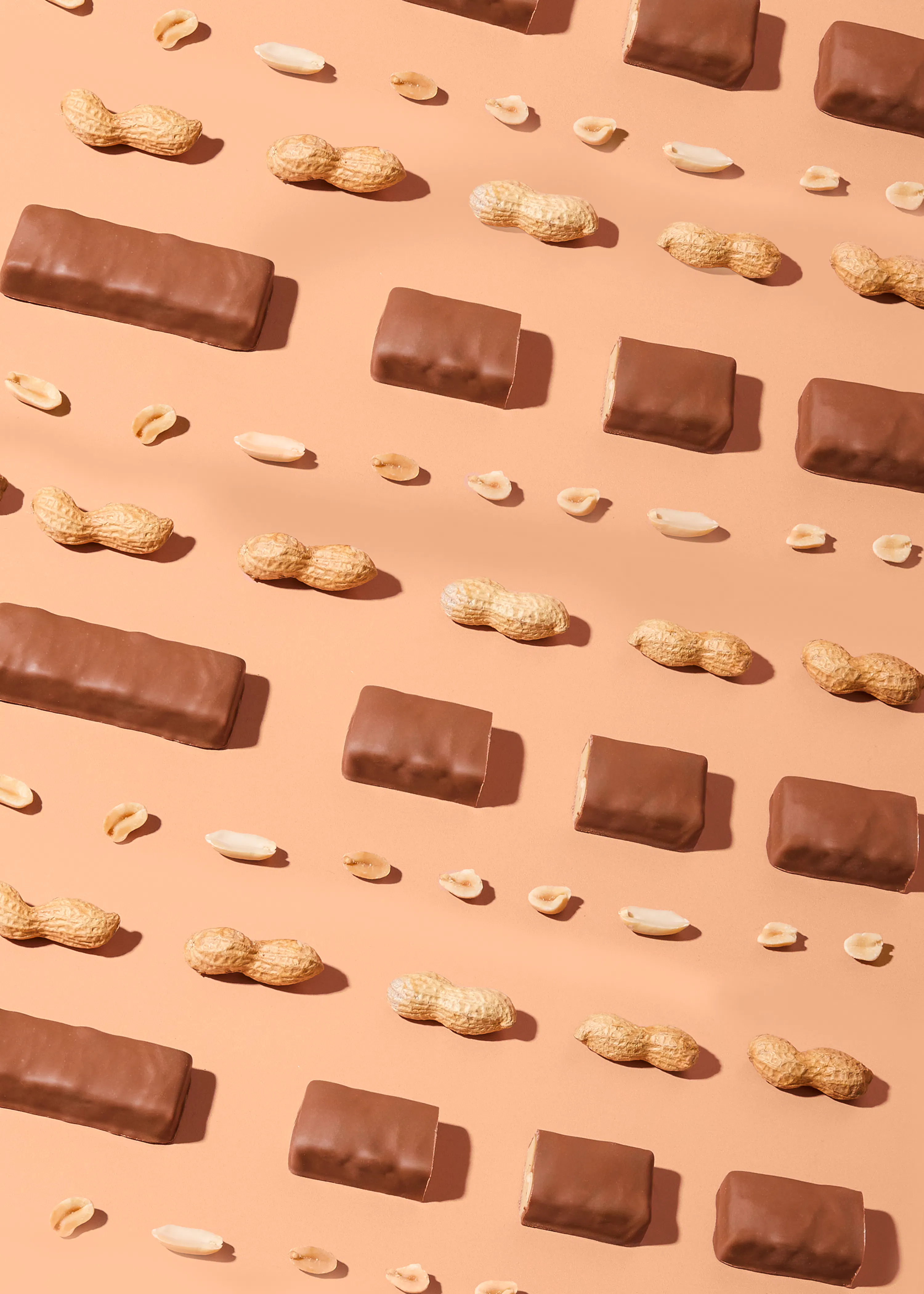 un motivo ripetuto di barrette di cioccolato e arachidi intere e sgusciate su uno sfondo marrone chiaro.