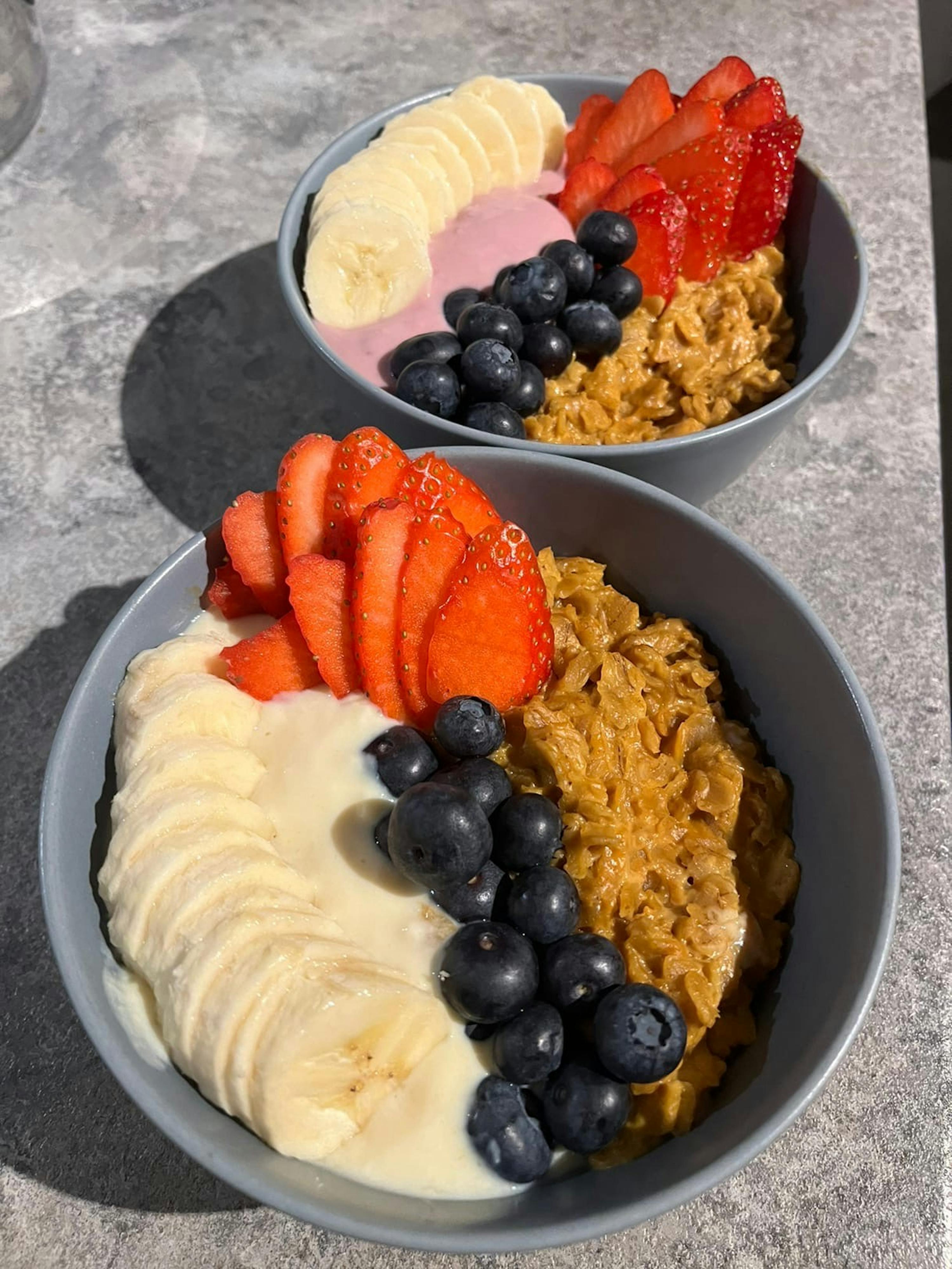 zwei Schüsseln Haferflocken mit Bananen , Blaubeeren und Erdbeeren