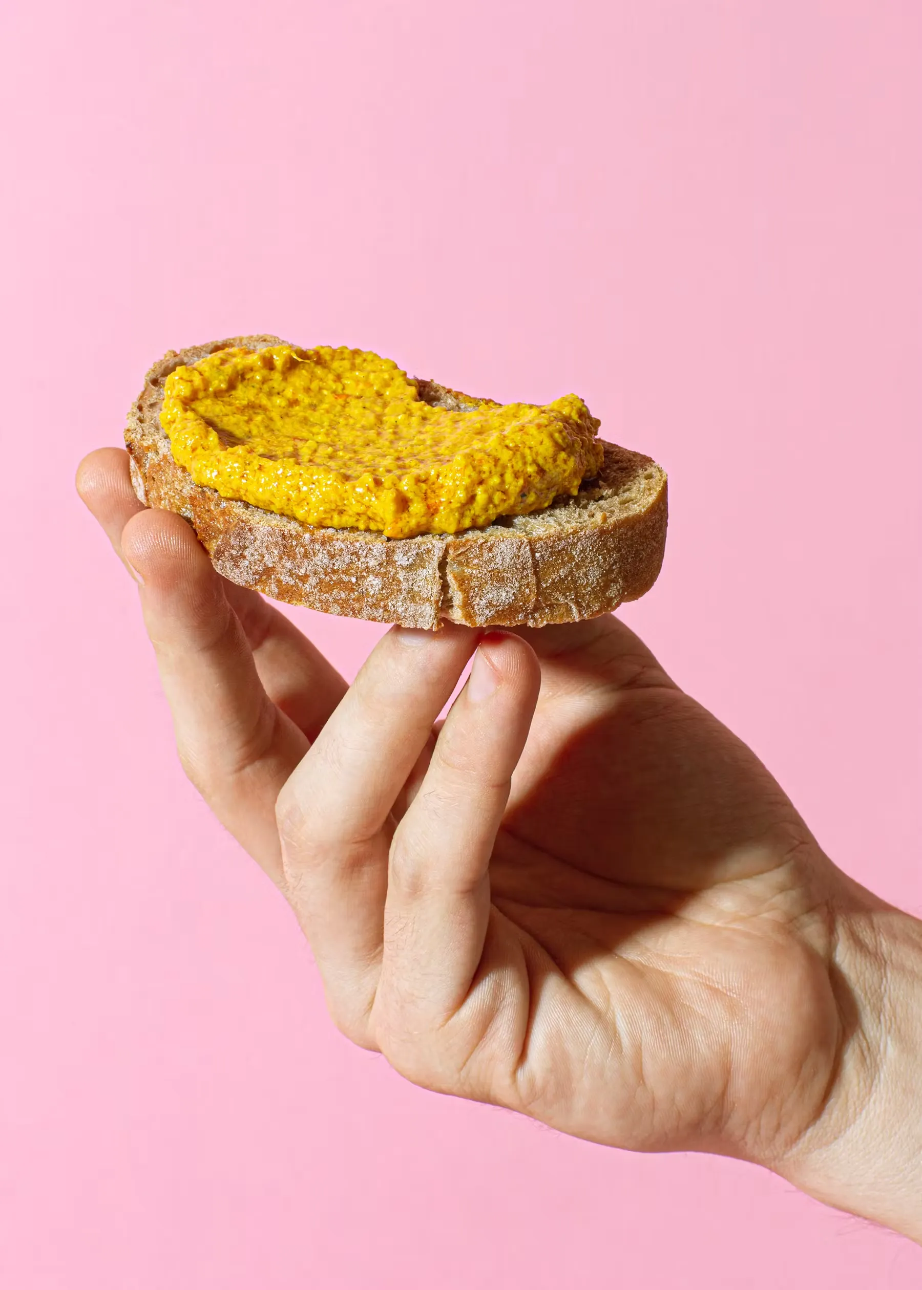 a hand holding a piece of bread with mustard on it