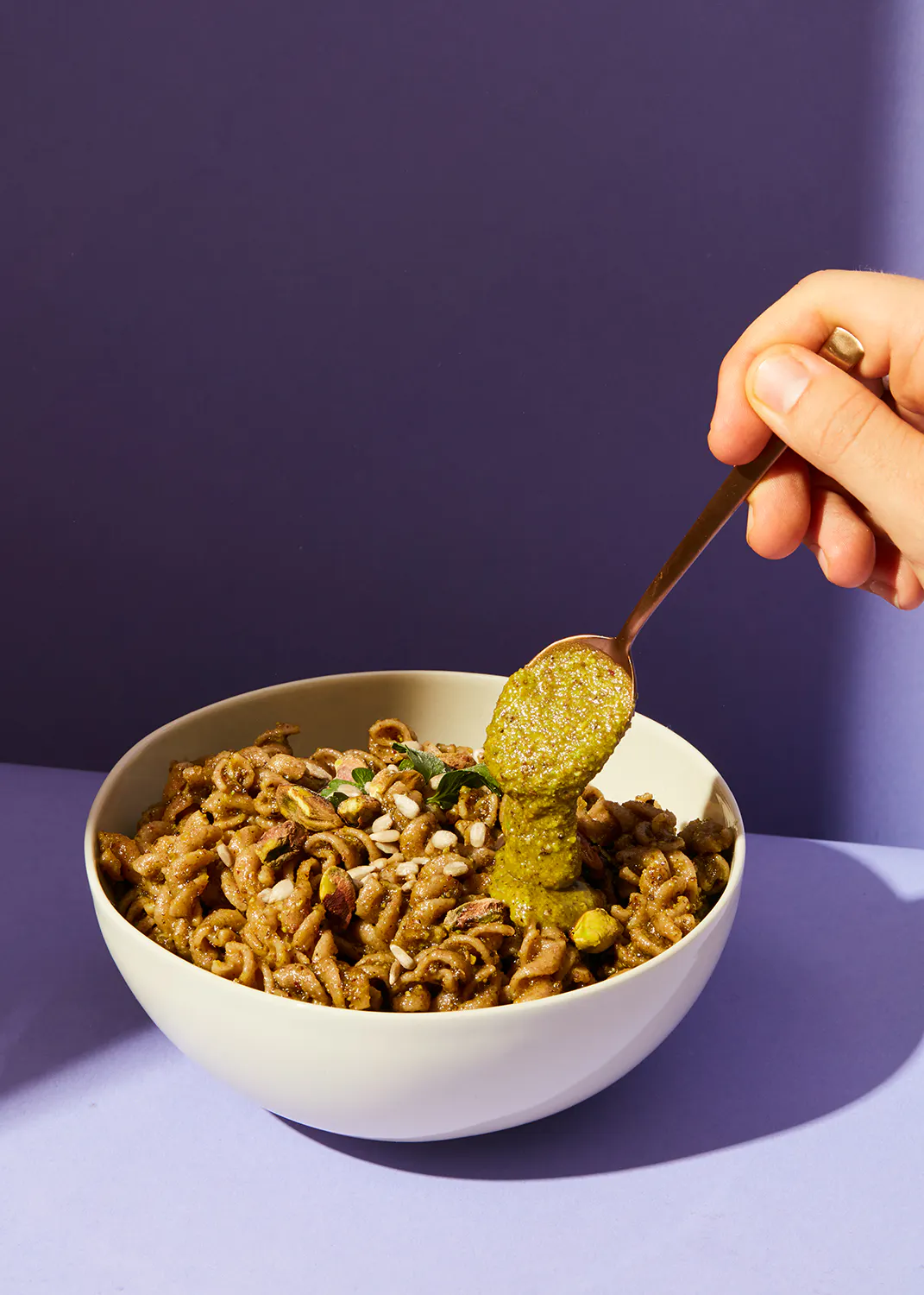 une personne verse du pesto sur un bol de pâtes avec une cuillère