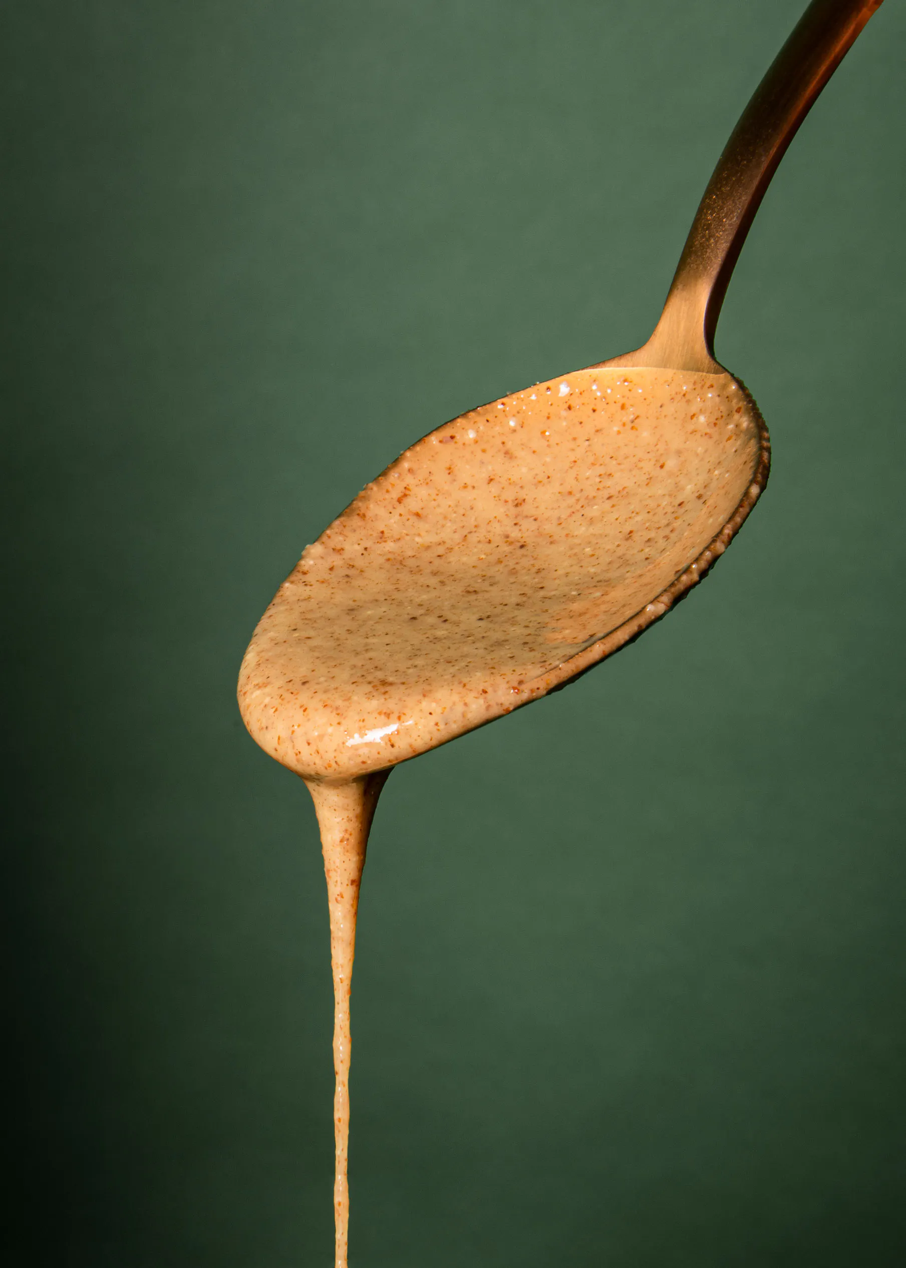 a spoon with a brown liquid pouring out of it on a green background