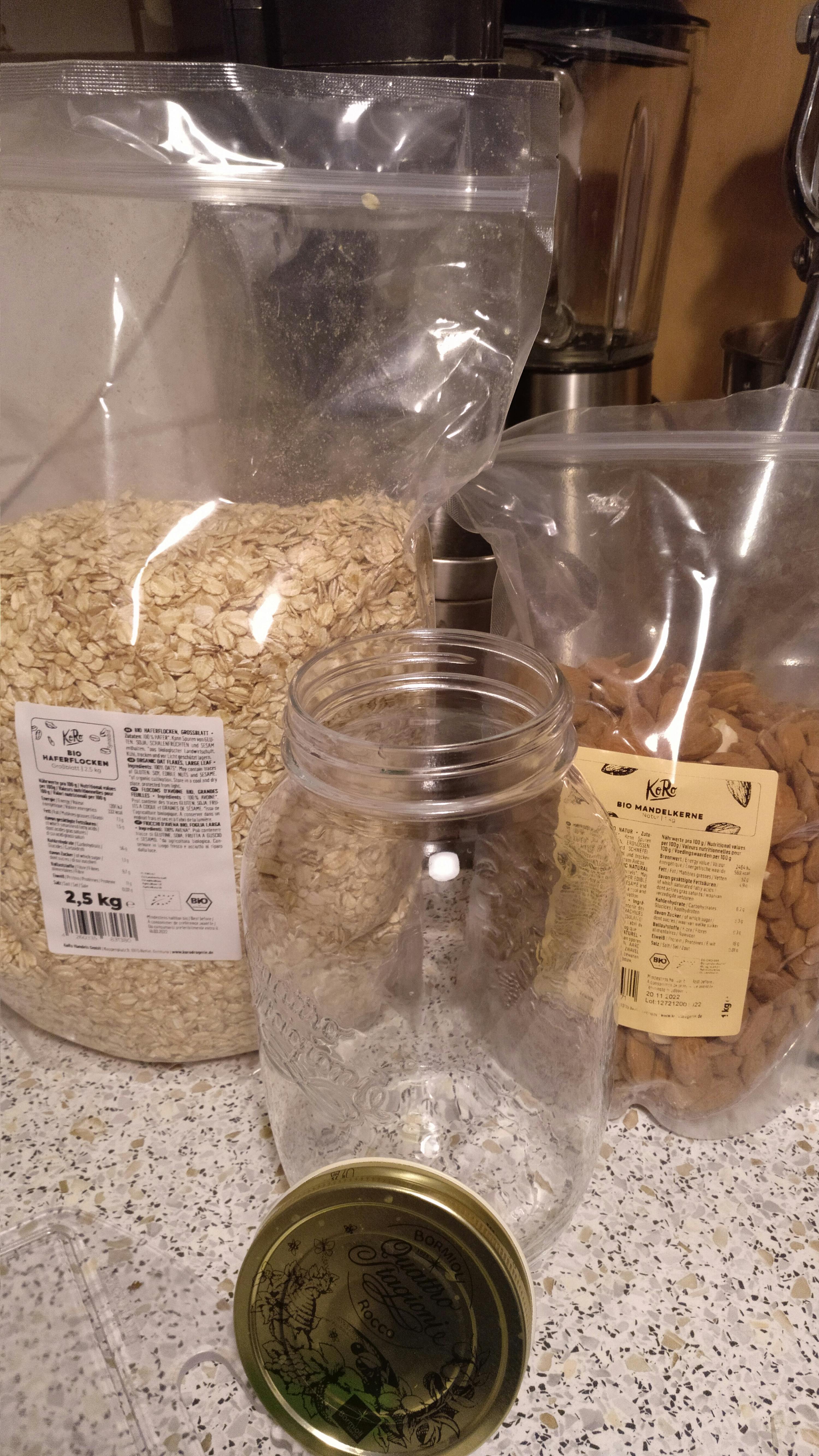 ein Glas mit einem goldenen Deckel steht neben einer Tüte Haferflocken und Mandeln