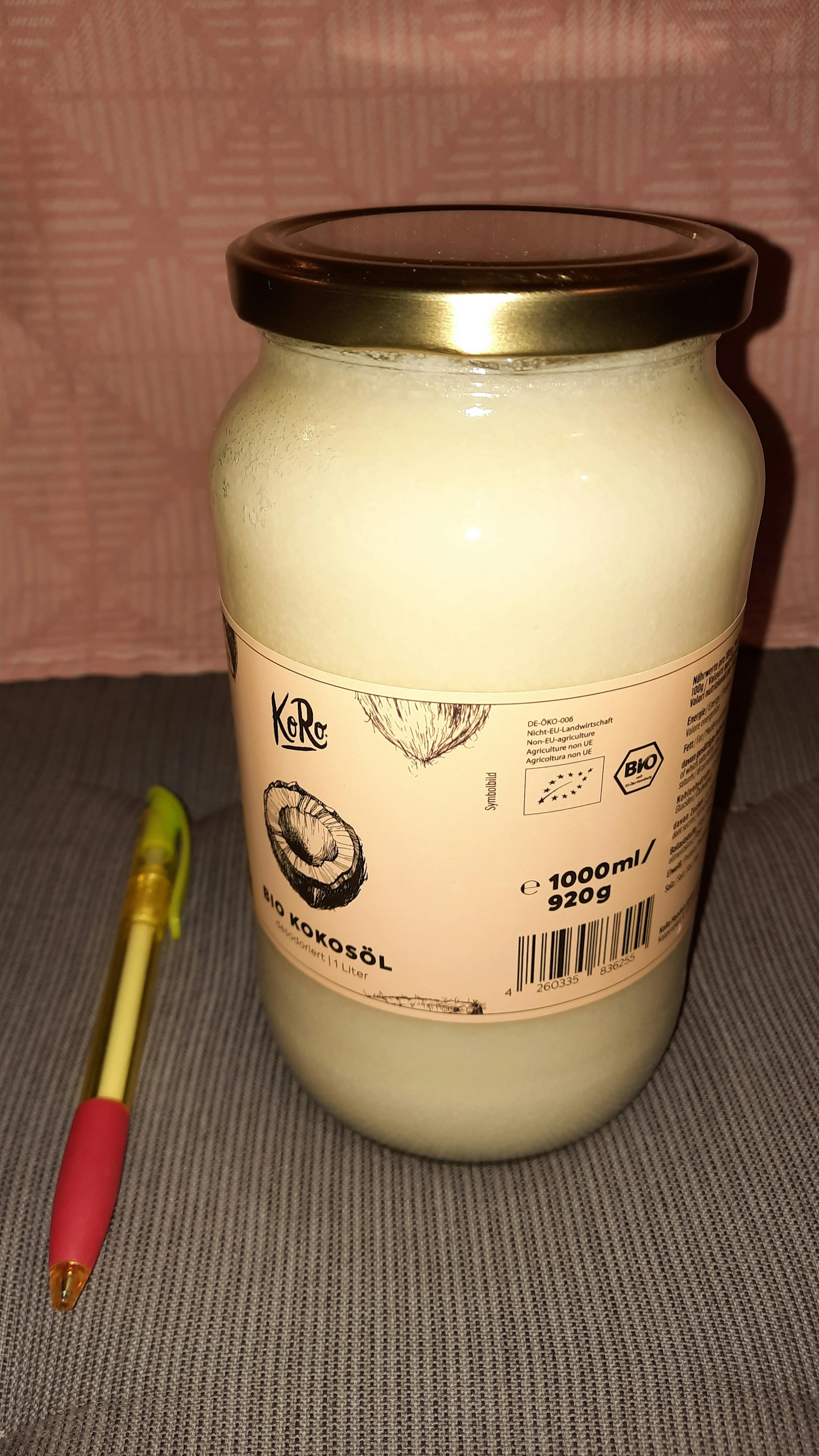 a jar of coconut oil sits on a table next to a pen