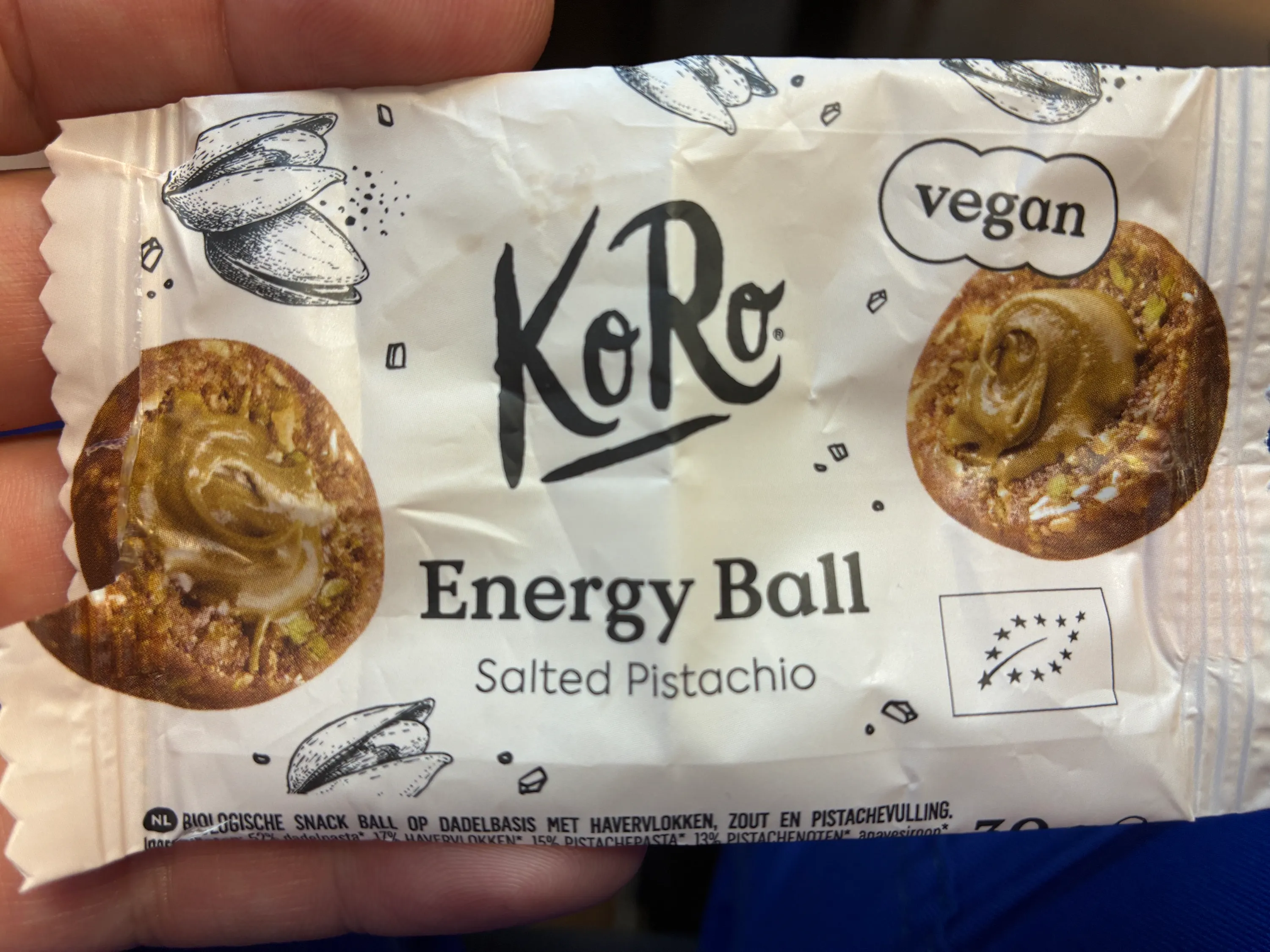 verpackung eines koro energy ball salted pistachio snacks, die das logo, die aufschrift „vegan“ und das eu-bio-siegel sowie abbildungen von pistazien und energiekugeln zeigt.