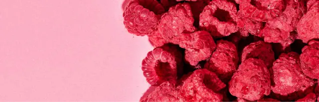 des framboises séchées rouges et texturées sur un fond rose uni.