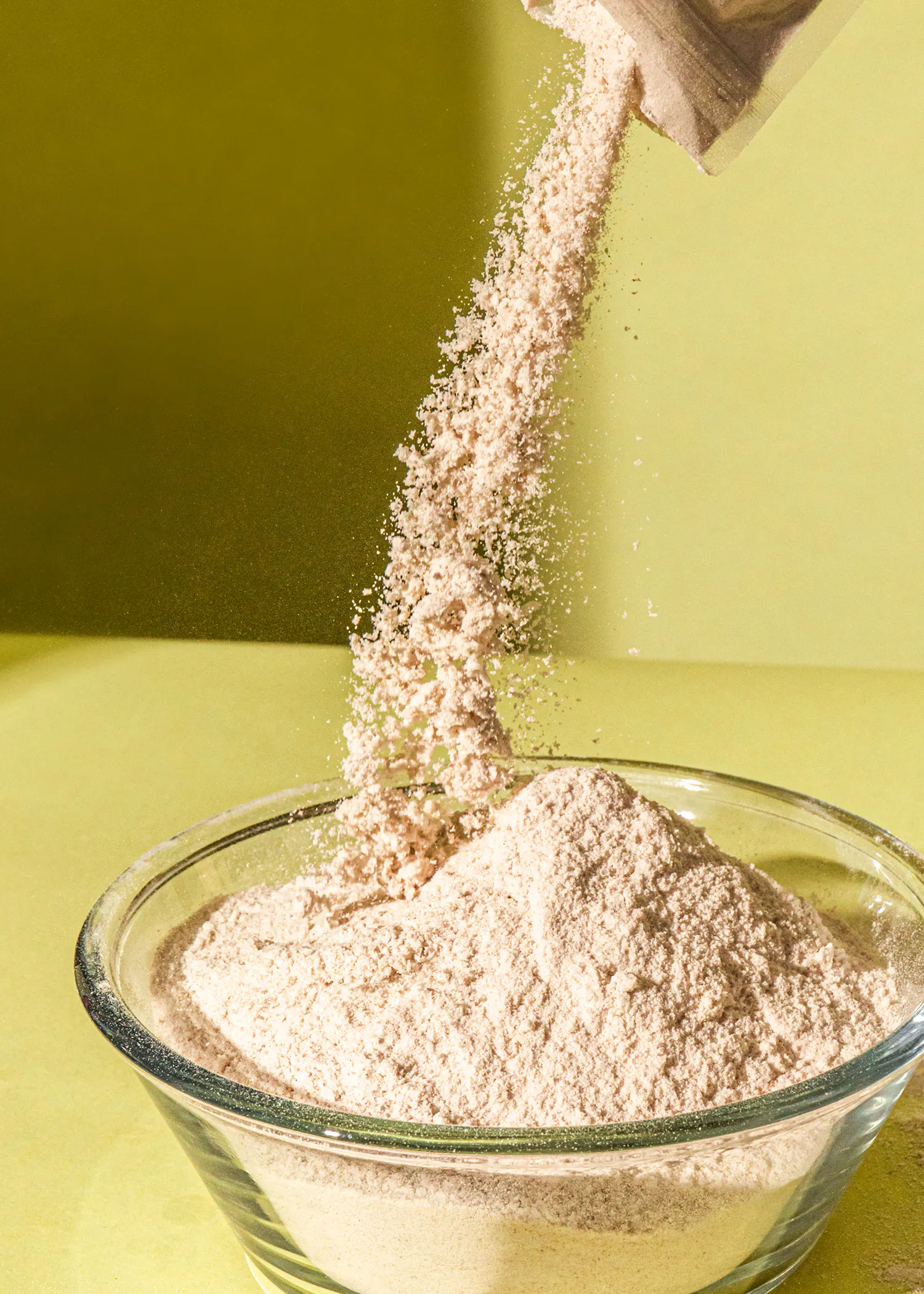 eine Glasschüssel mit braunem Mehl wird aus einem Plastikbeutel gegossen