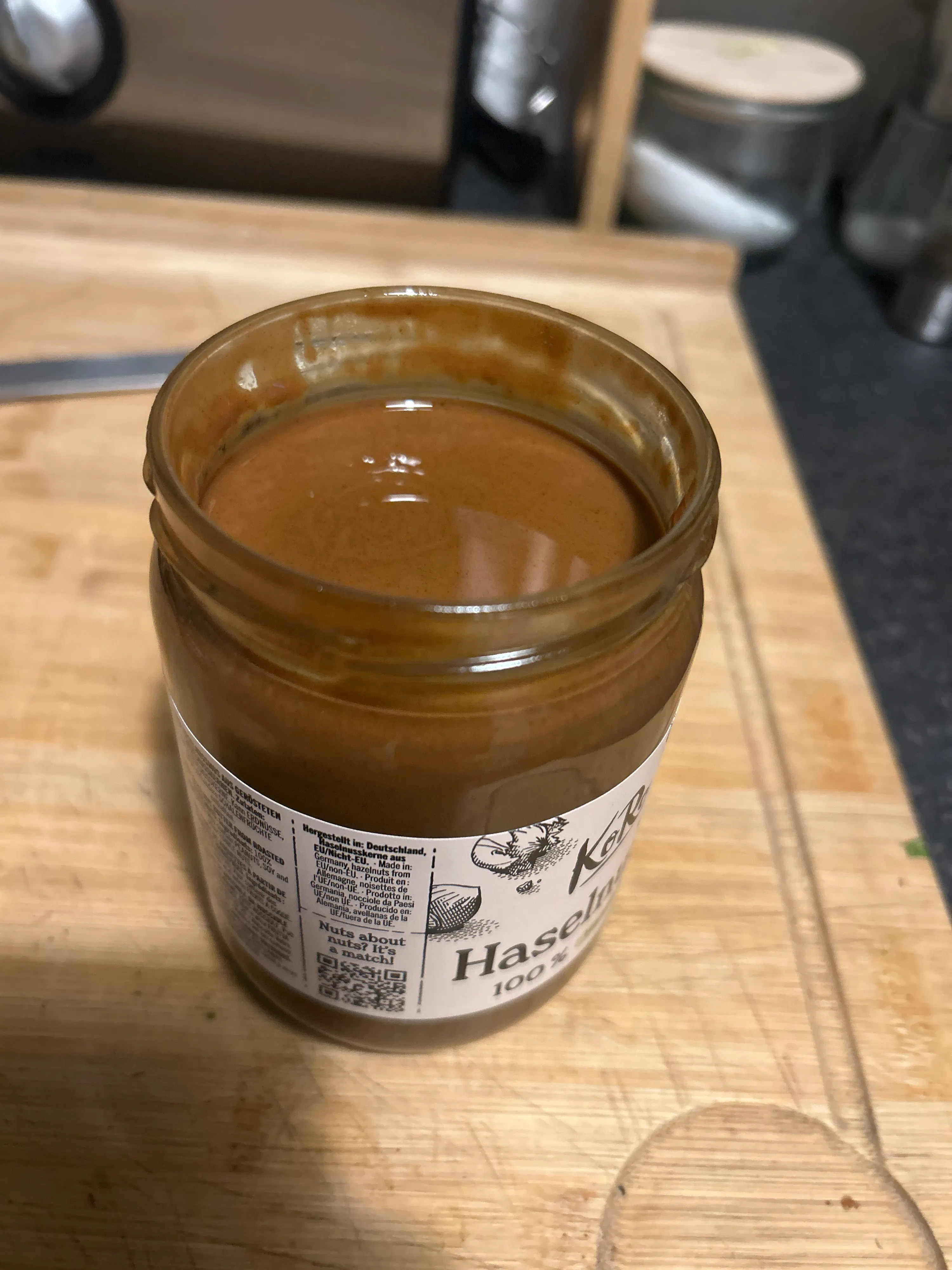 ein offenes glas haselnussmus auf einem holzschneidebrett, das eine glatte, hellbraune paste zeigt.