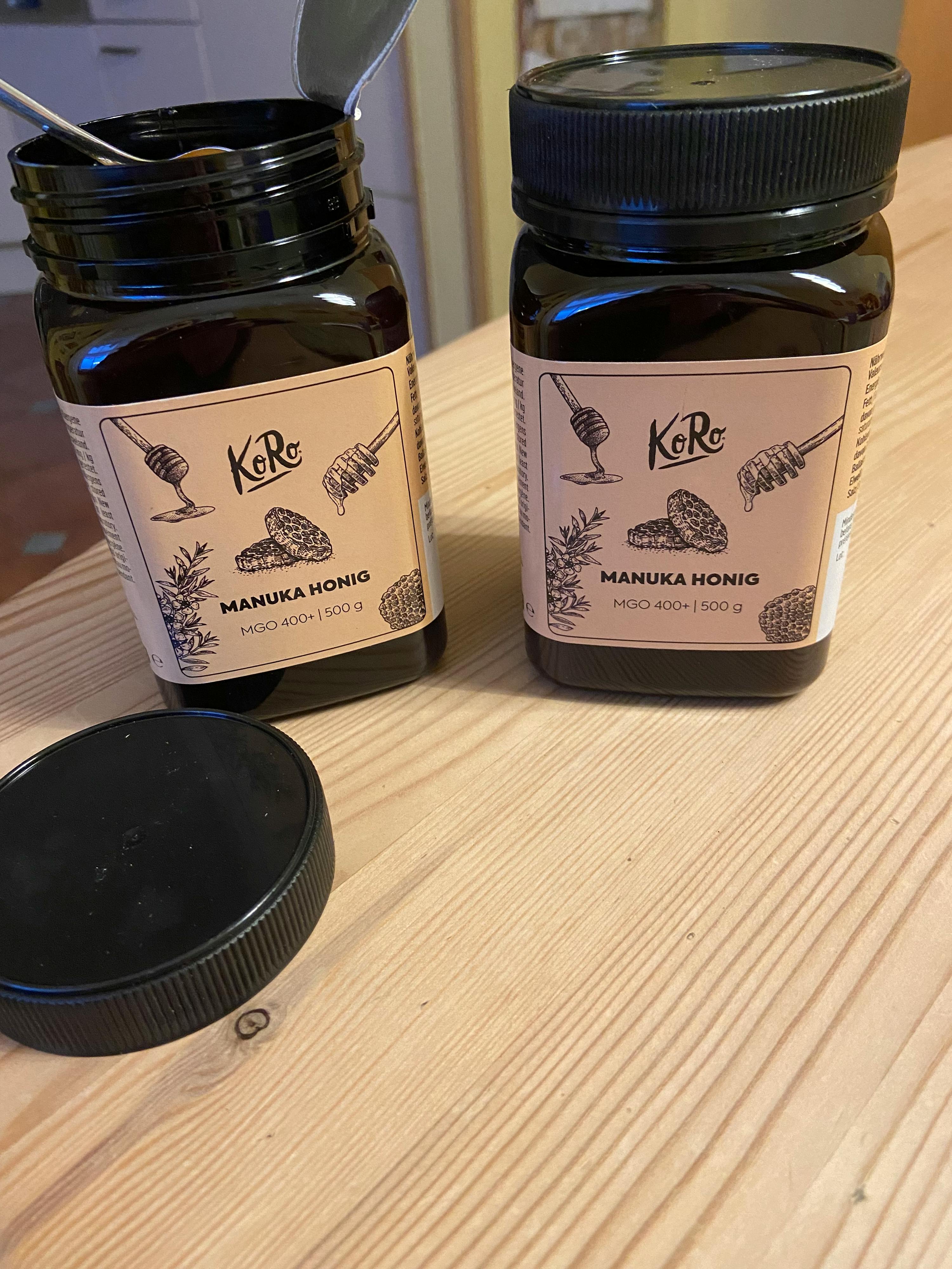 two jars of manuka honig sit on a wooden table