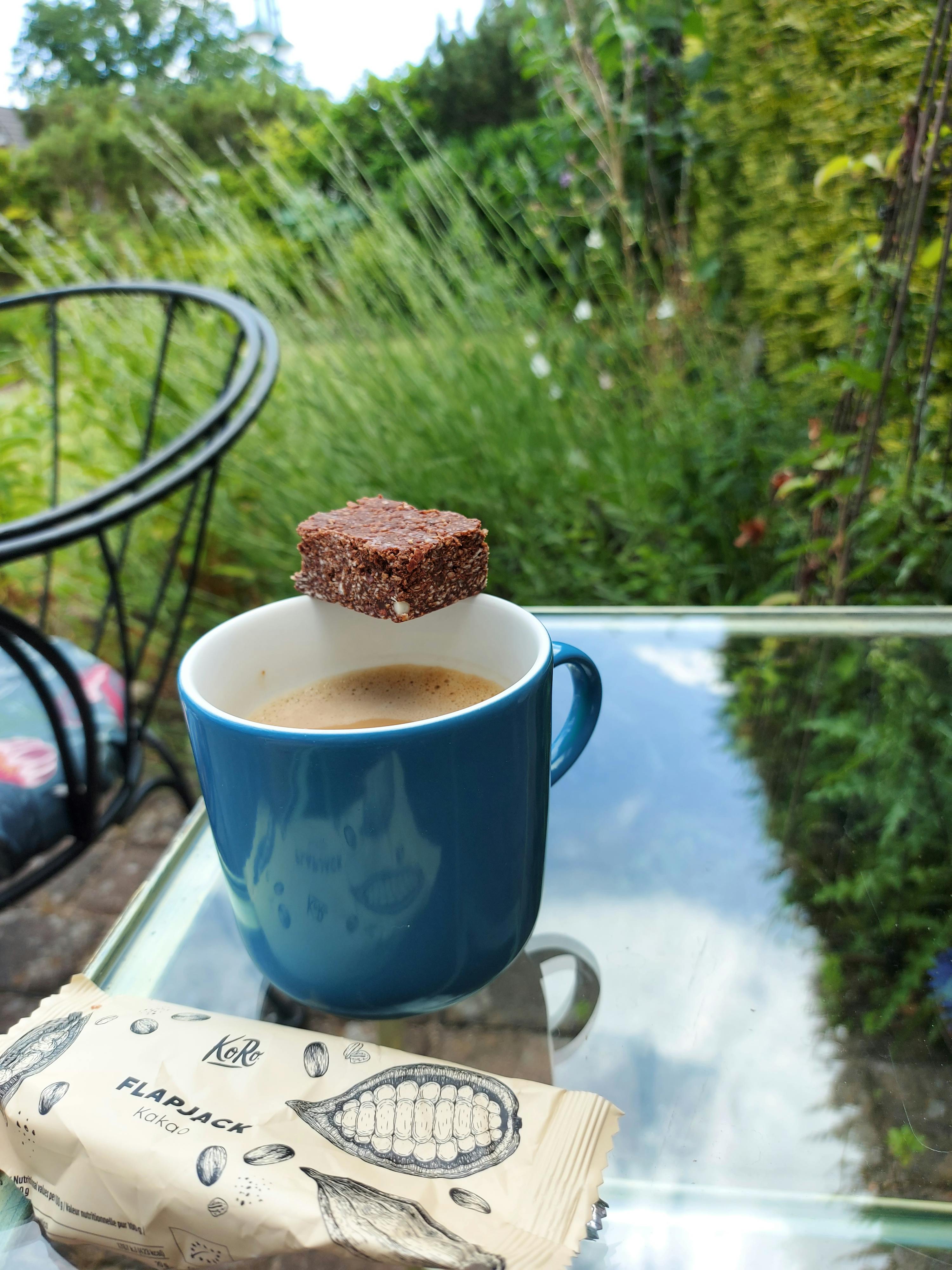 une tasse de café bleue sur une table à côté d' un paquet de flapjack