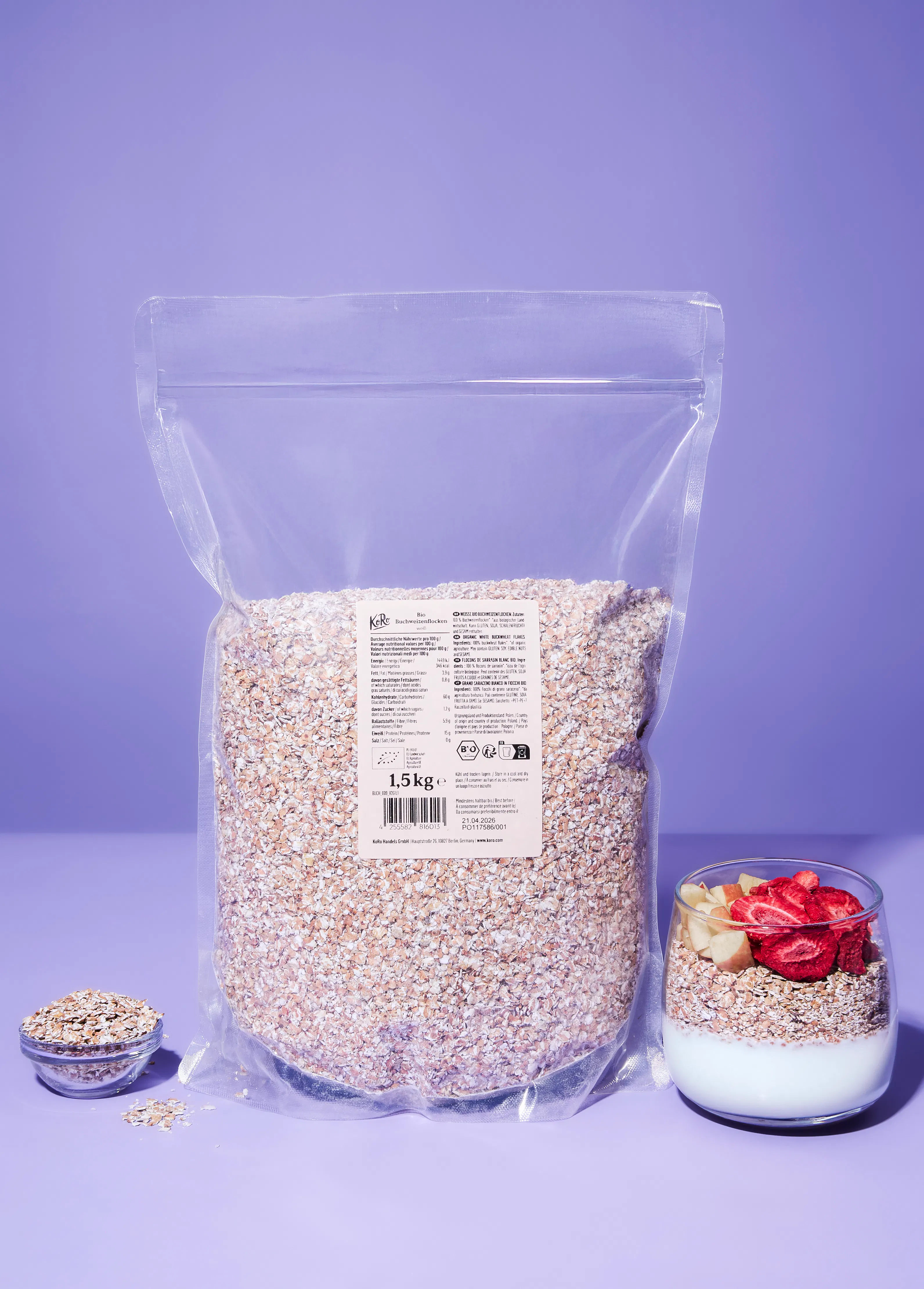 un grand sac transparent de 1,5 kg de flocons de sarrasin bio est posé sur une surface violette, avec un petit bol de flocons à gauche et un verre de yaourt, flocons et fruits coupés à droite.