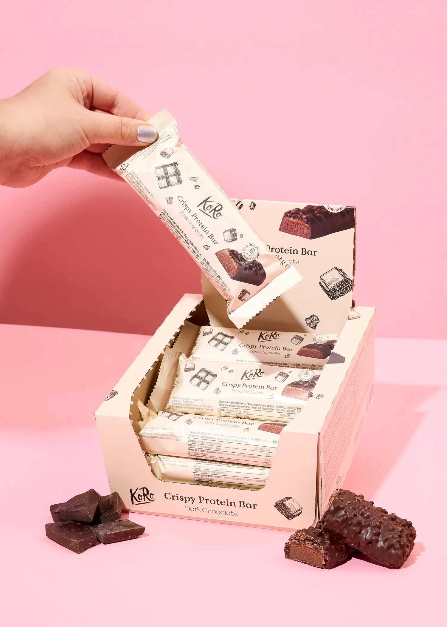 une personne tient une barre de protéines croustillante sur une table rose