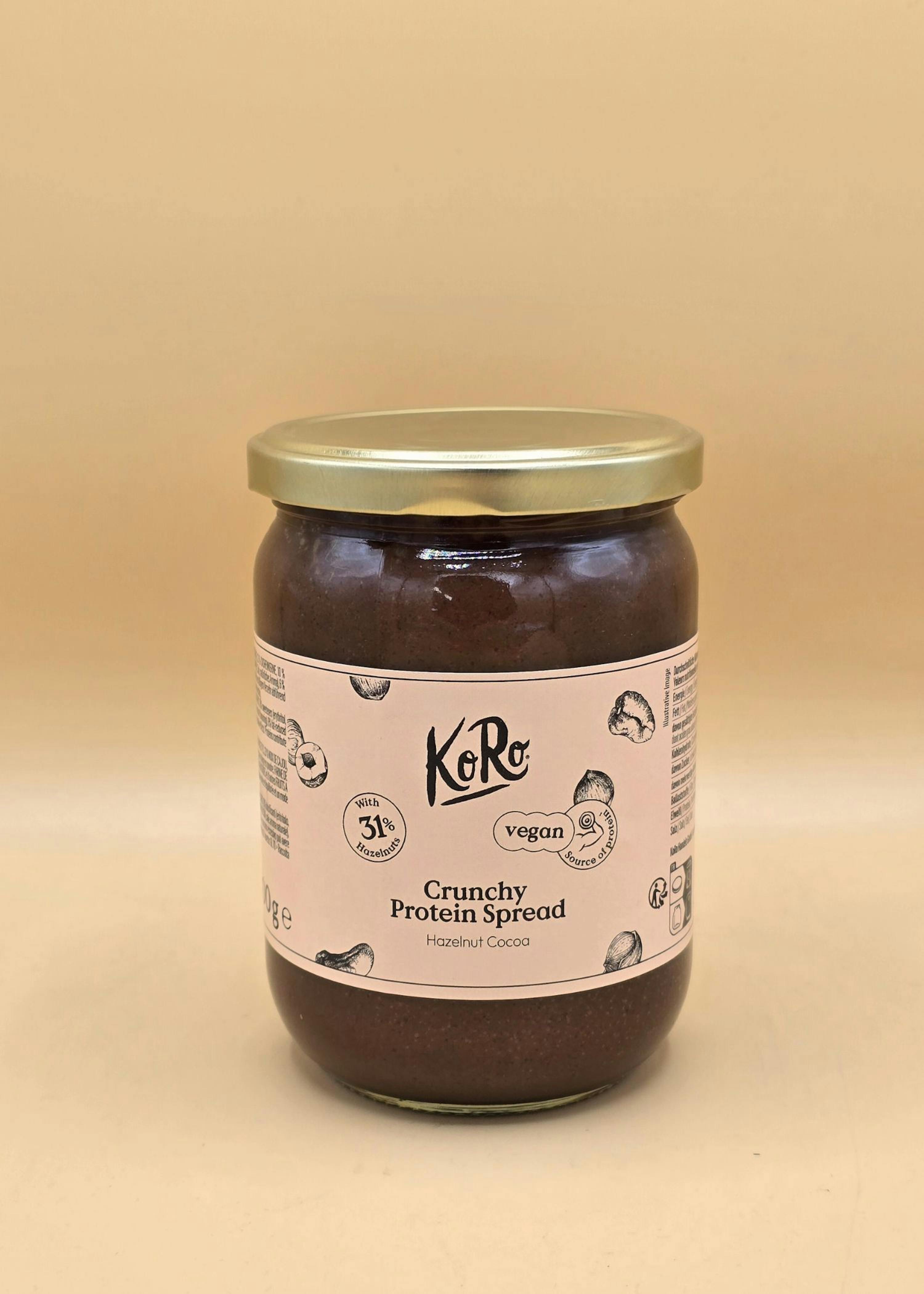 un barattolo di crema proteica croccante al cacao e nocciole koro con il 31% di nocciole, vegana e fonte di proteine, su sfondo beige.