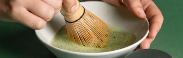 une personne mélange un bol de thé vert avec un fouet en bois