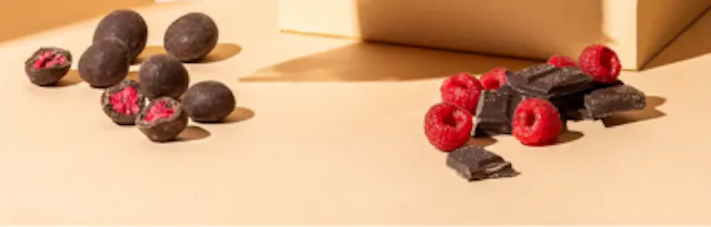 schokoladenüberzogene himbeeren und stücke dunkler schokolade mit frischen himbeeren auf einem hellbraunen hintergrund.