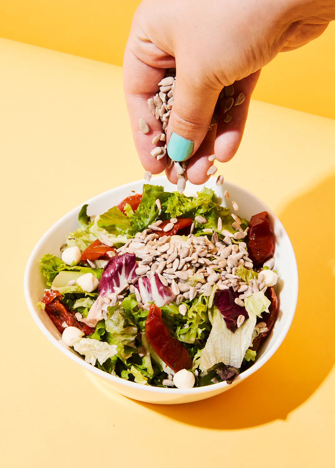 une personne versant des graines de tournesol dans un bol de salade
