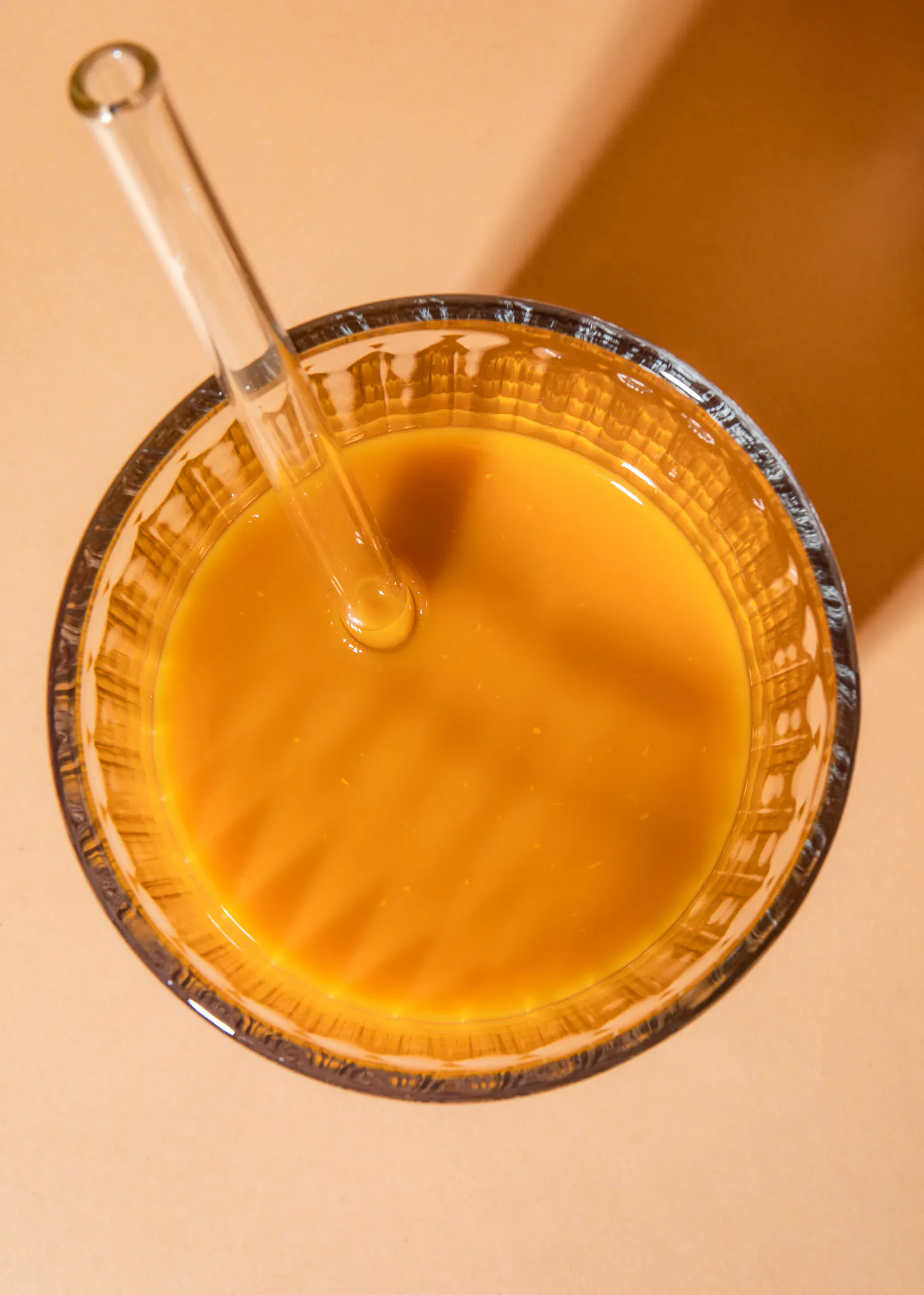 a glass of orange liquid with a clear straw in it
