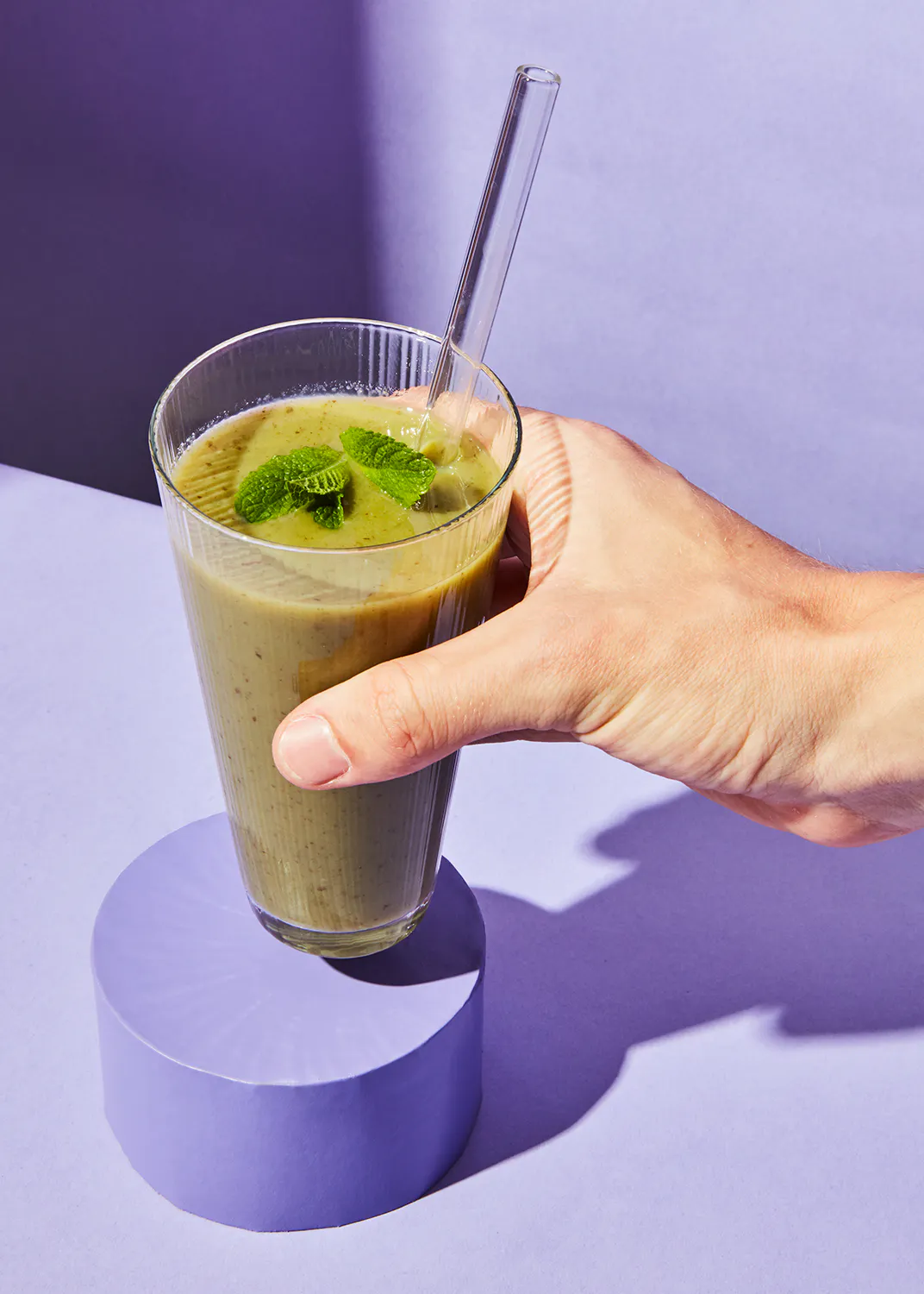 une personne tient un verre de smoothie vert avec une paille