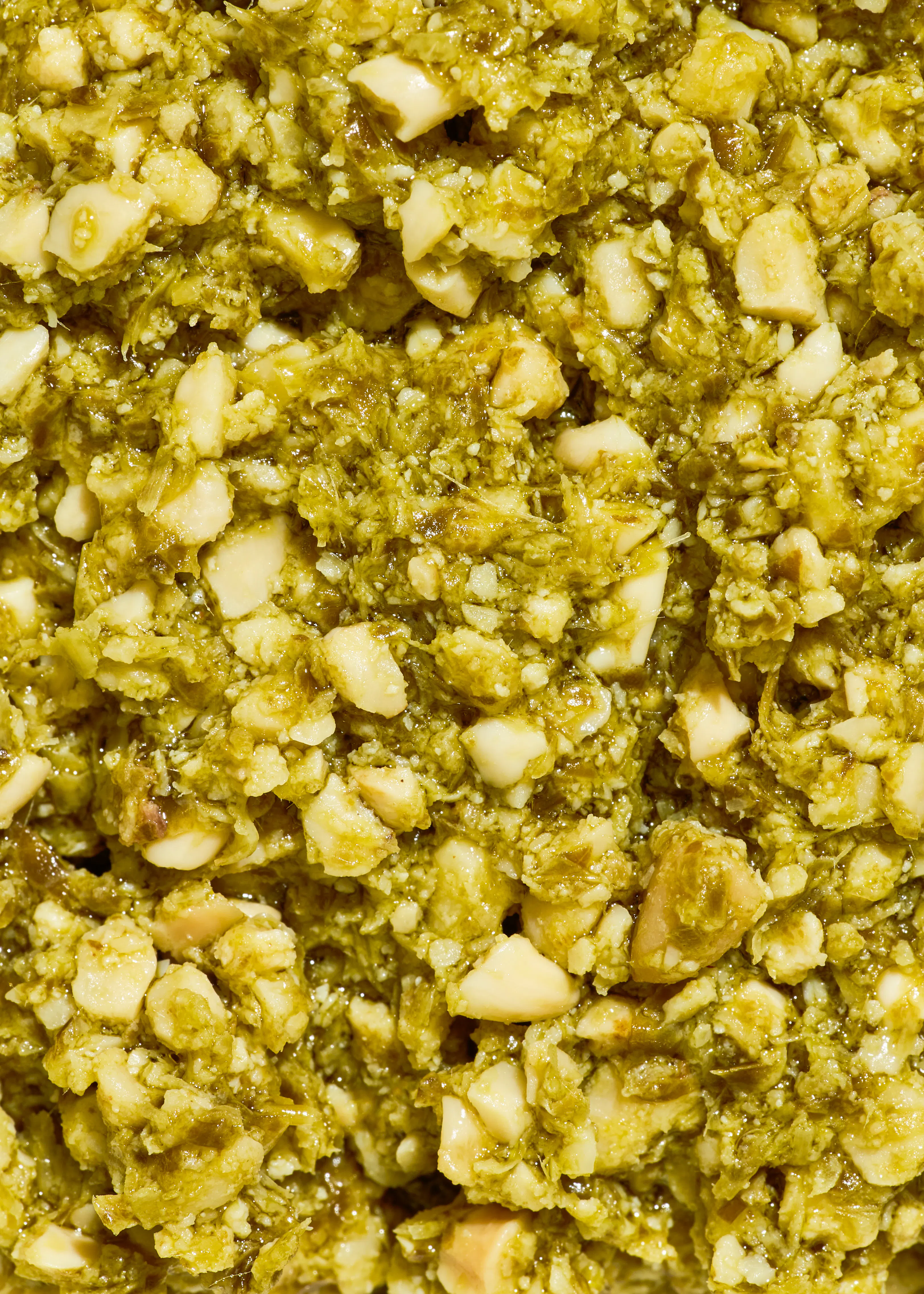 gros plan sur une texture granuleuse et humide de pesto vert avec des morceaux de noix clairs.