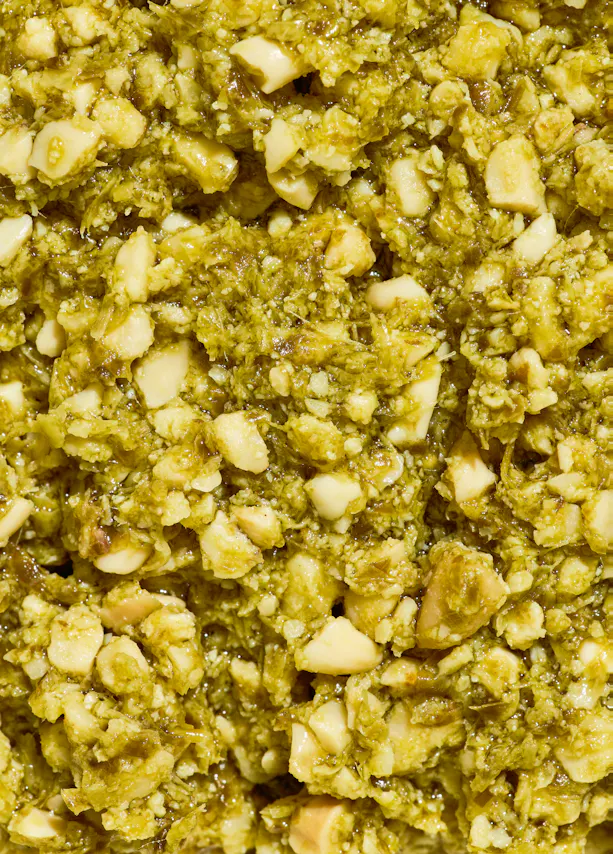 gros plan sur une texture granuleuse et humide de pesto vert avec des morceaux de noix clairs.