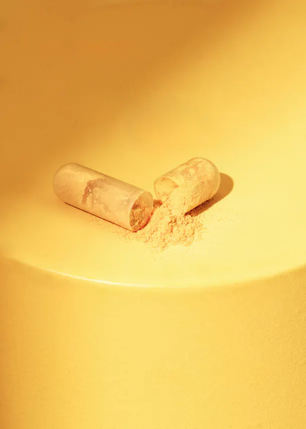 a capsule with powder poured out of it on a yellow surface