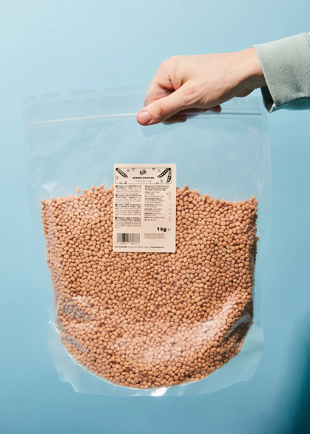 eine Person hält einen Plastikbeutel mit braunen Linsen in der Hand
