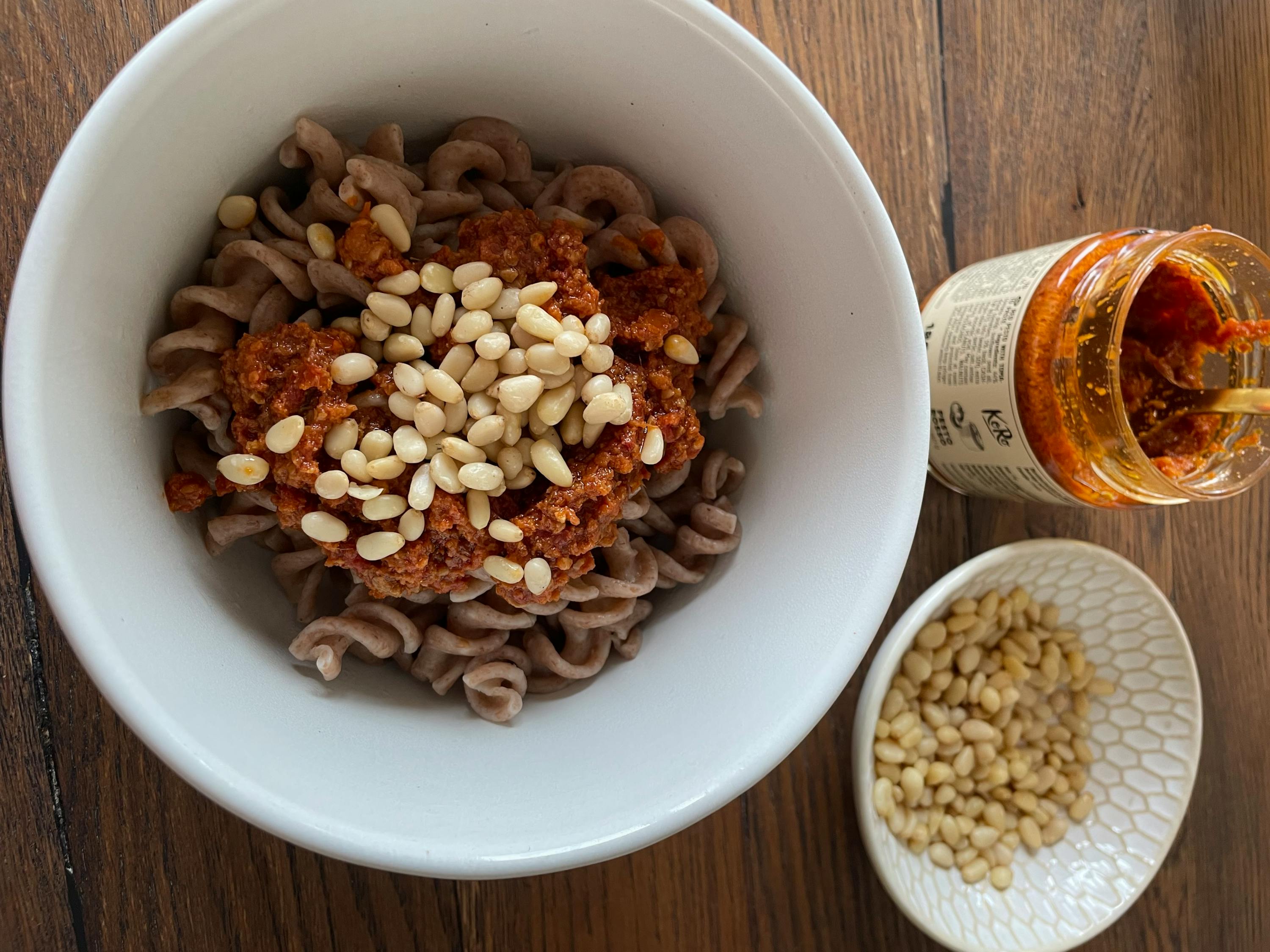 una ciotola di pasta con pinoli e un barattolo di salsa