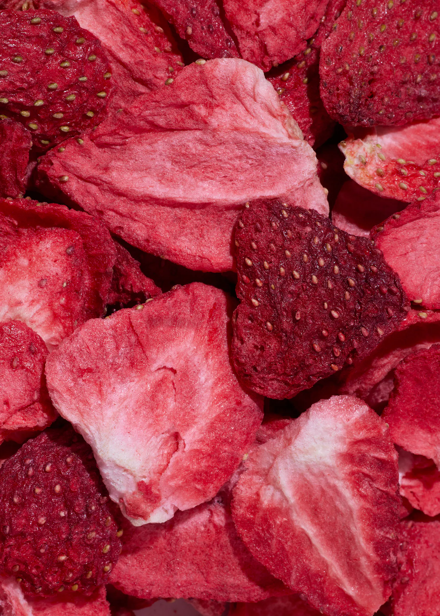 nahaufnahme von gefriergetrockneten erdbeeren, die sowohl ganze früchte als auch geschnittene stücke mit sichtbaren samen zeigen.