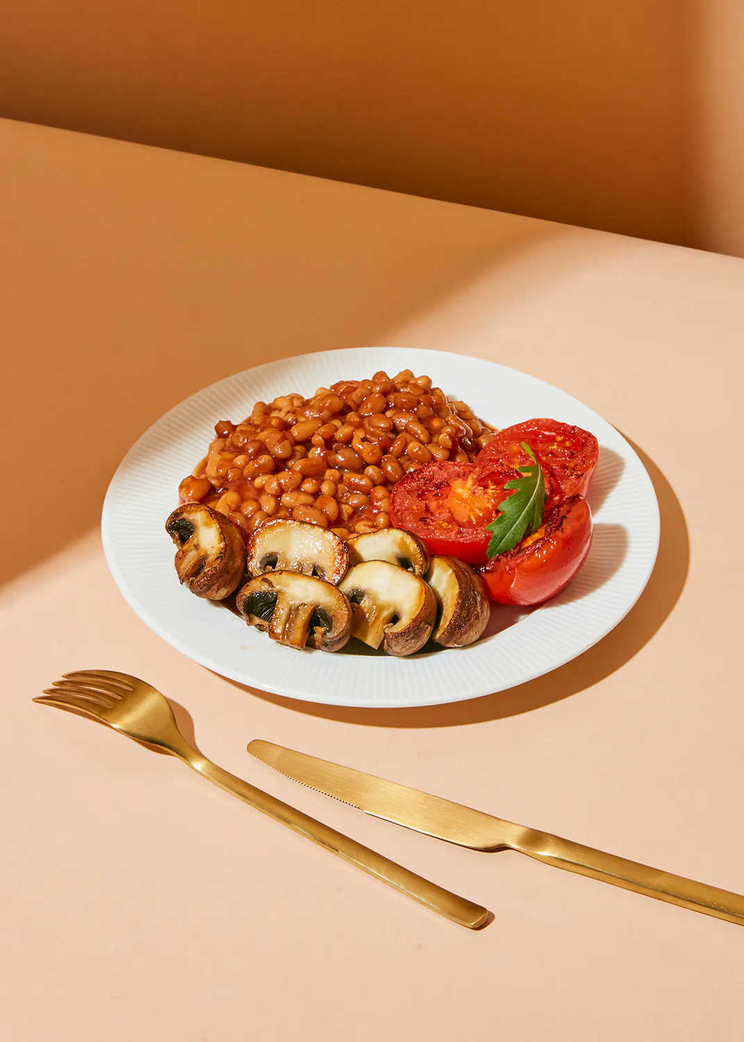 ein weißer Teller mit Bohnen Pilzen und Tomaten auf einem Tisch