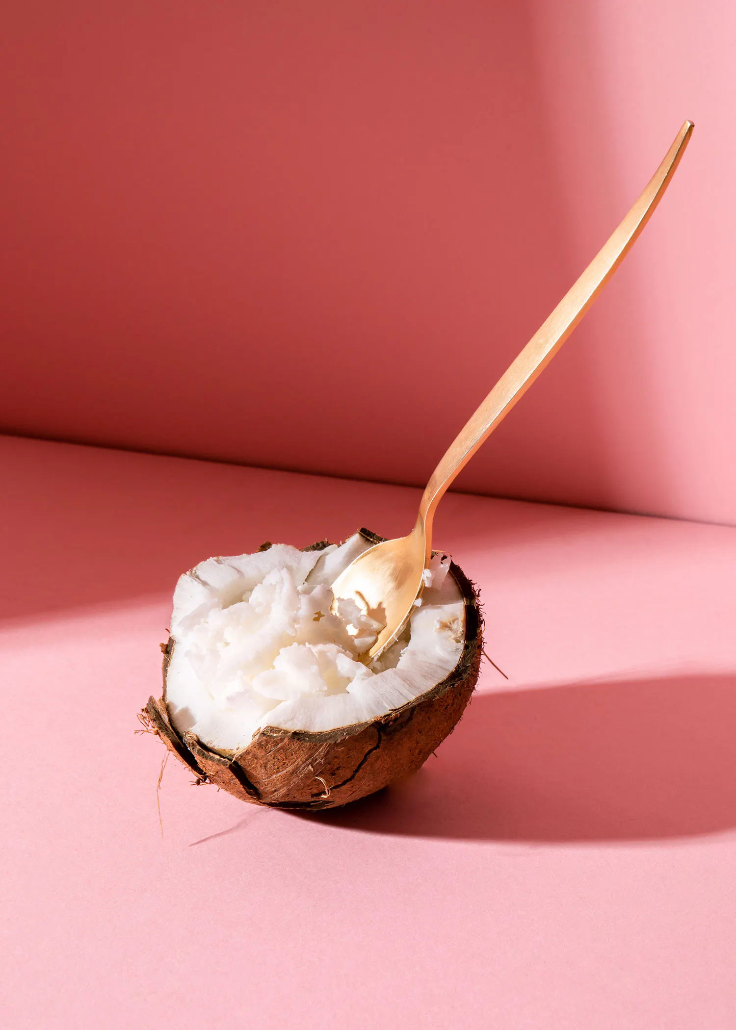 a spoon is sticking out of a coconut on a pink background