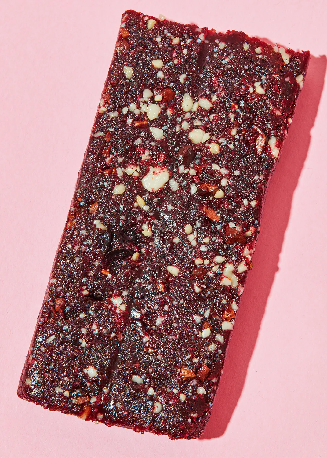 une barre de chocolat rouge avec des noix sur fond rose