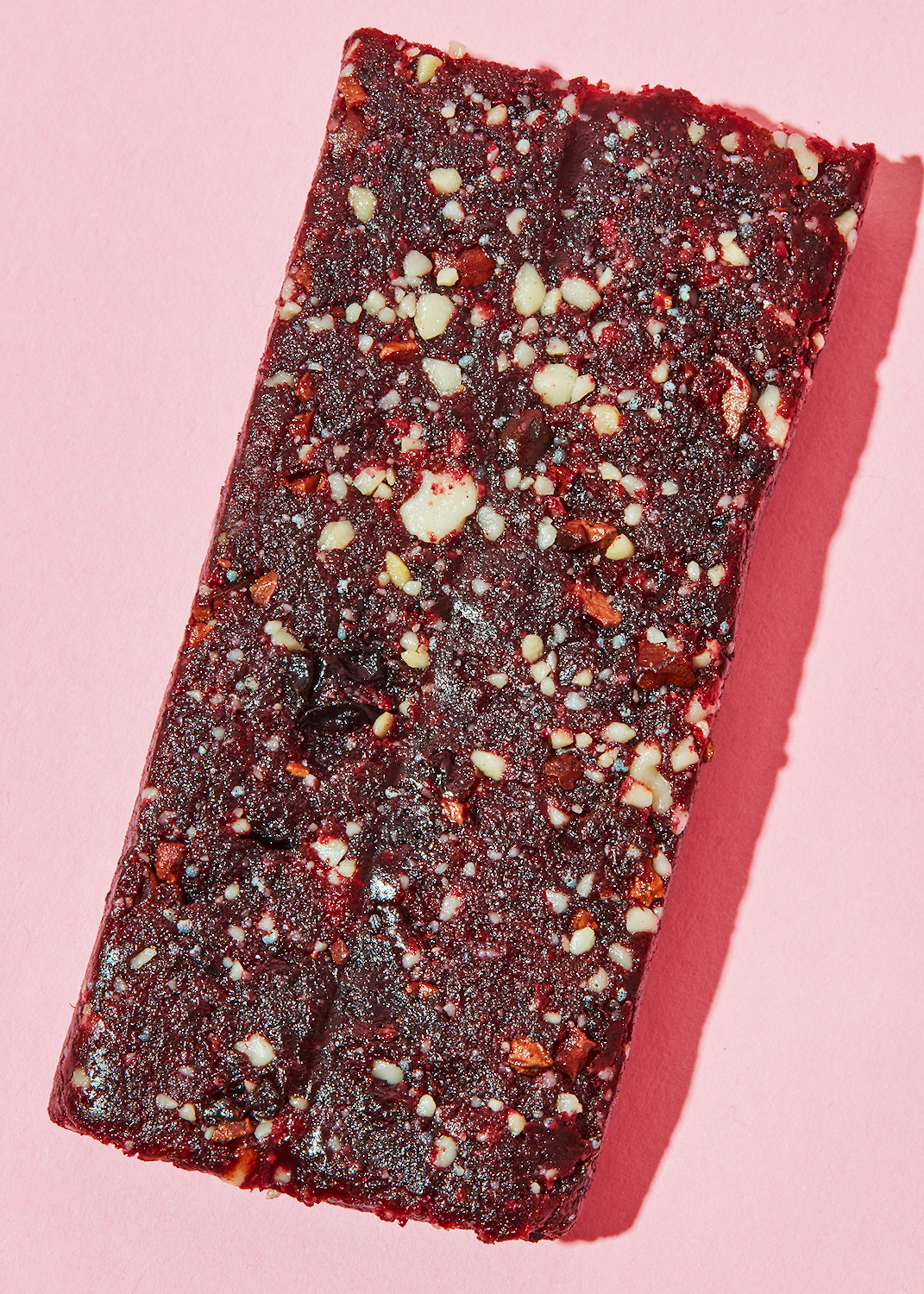 eine rote Bar mit Nüssen und Schokoladenstückchen auf einem rosa Hintergrund