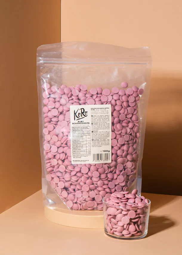 ein Plastikbeutel mit rosa Schokoladentropfen neben einem Glas