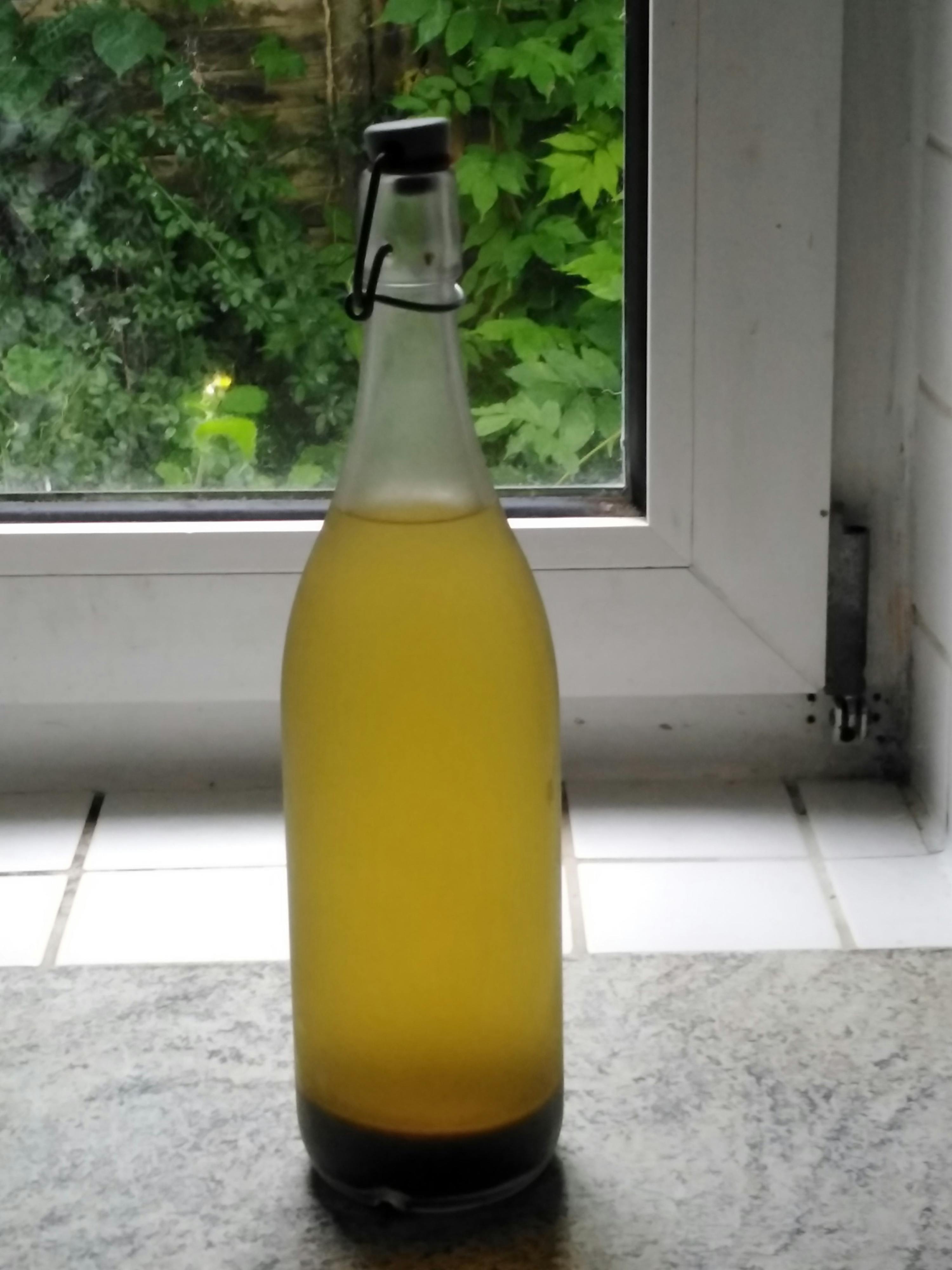 une bouteille de liquide jaune est assise sur un comptoir à côté d' une fenêtre